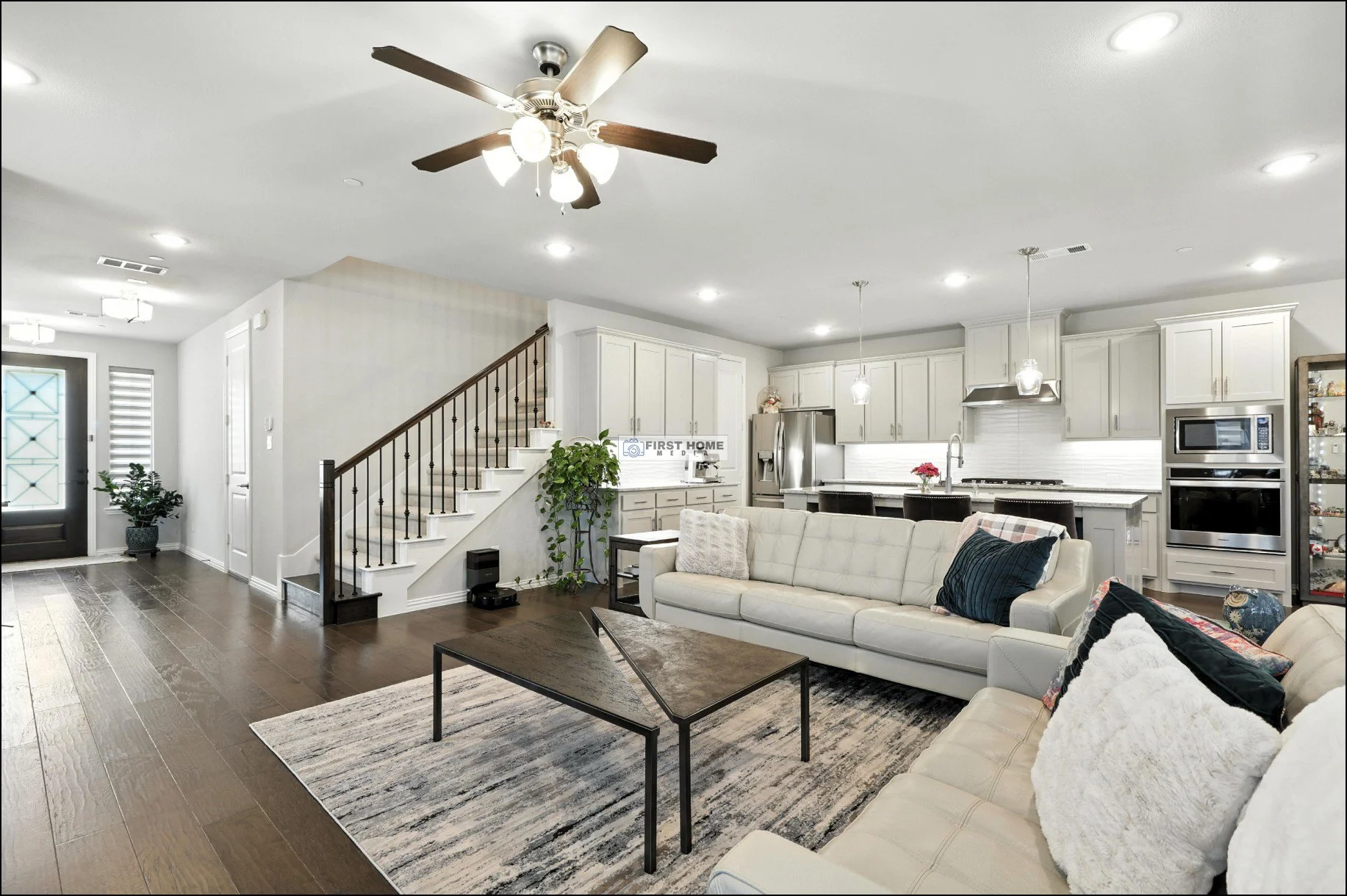 Open living room and kitchen area with hardwood floors, white sofas, a wooden coffee table, a ceiling fan, and modern appliances and cabinetry.
