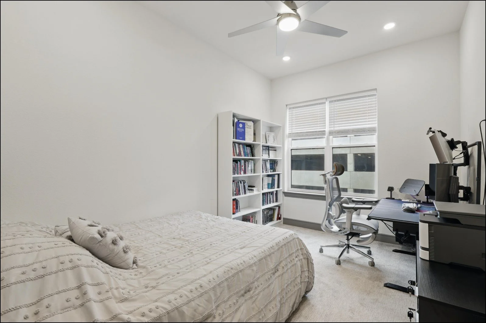 Modern bedroom with a bed, bookshelf, desk, chair, and computer setup