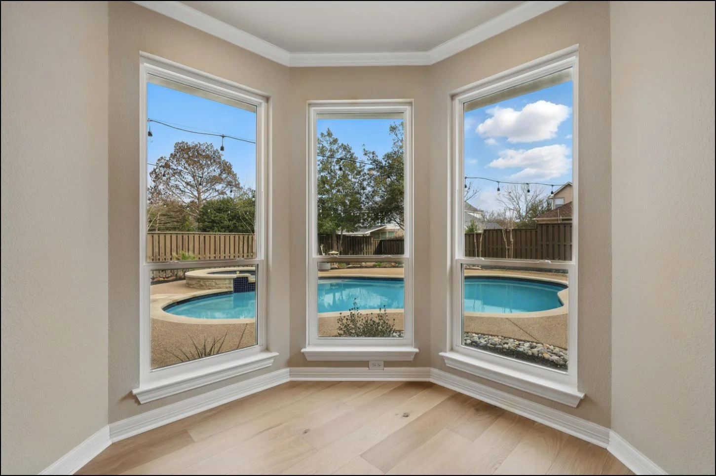 View through bay windows onto a backyard with a swimming pool.