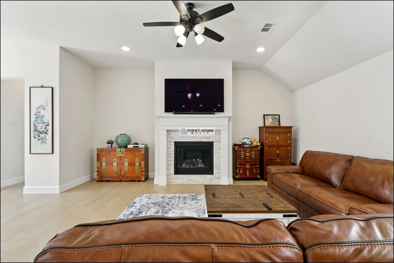 Living room with brown leather sofas, a white fireplace with a TV above, and various decorative furniture against light-colored walls.