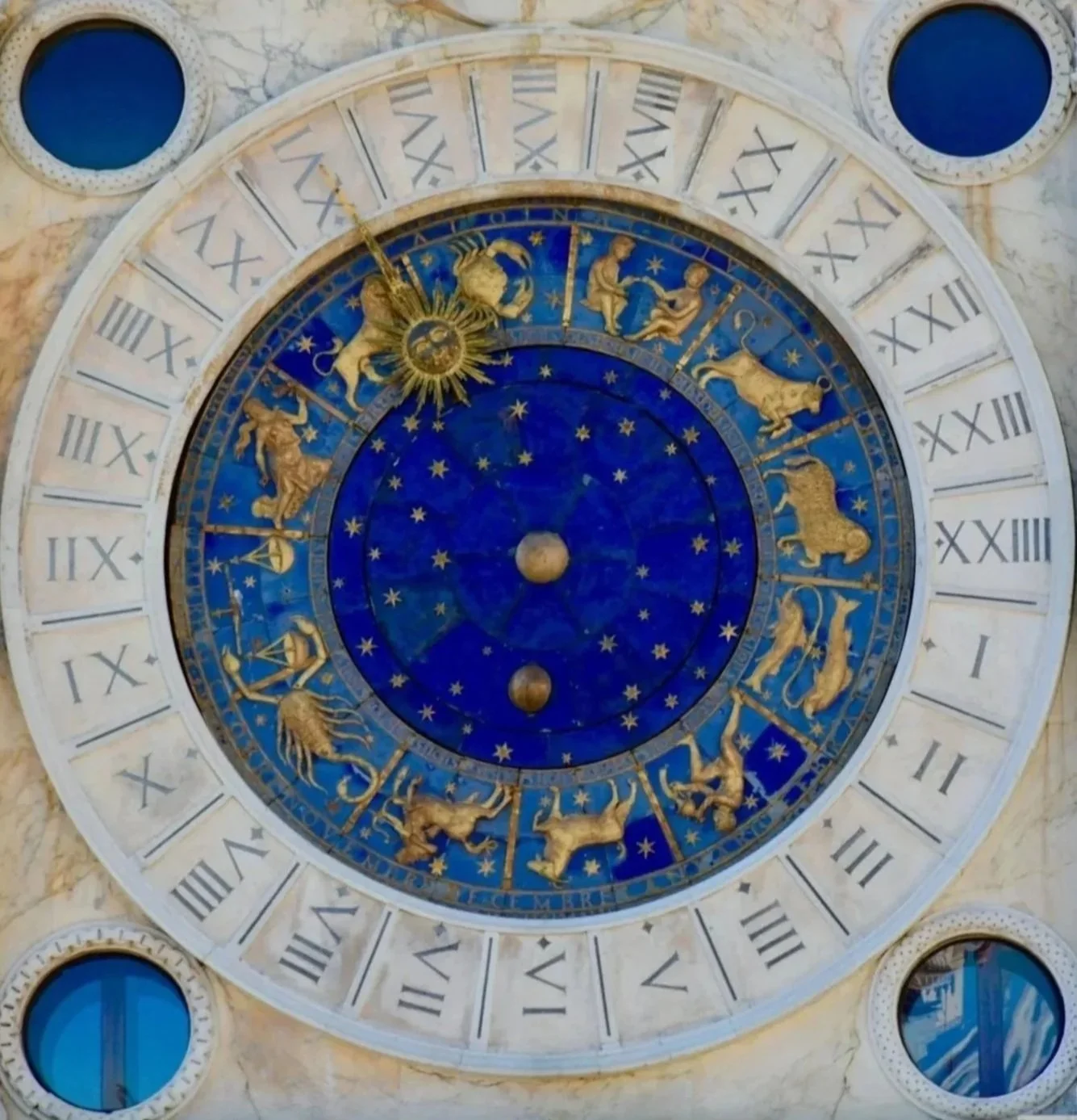 An ornate clock with zodiac signs and a blue background, featuring Roman numerals around the edge.