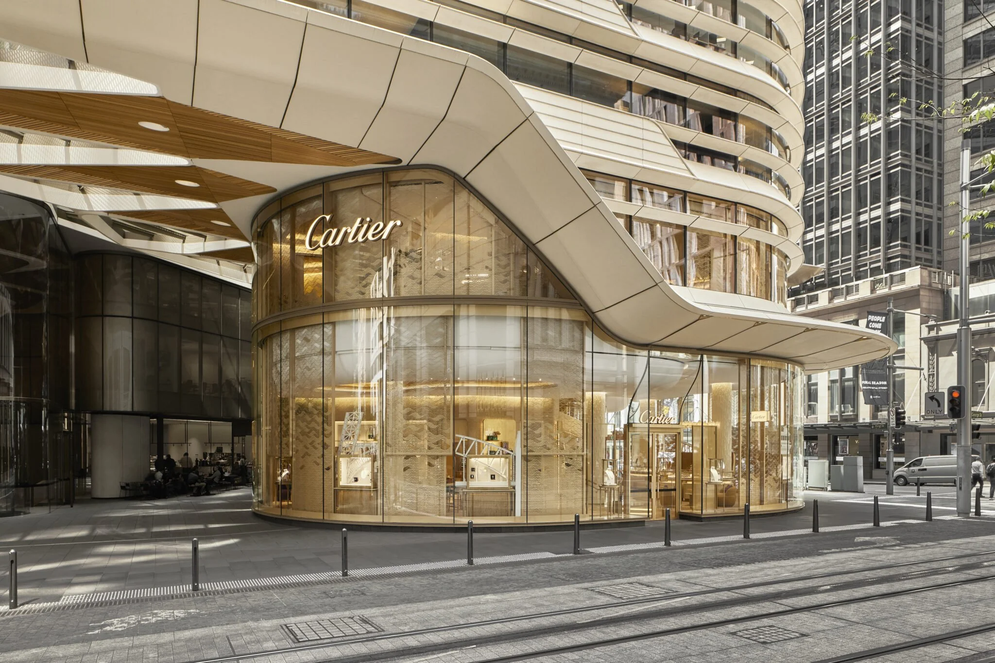 Exterior view of a modern luxury Cartier store with glass storefront, gold accents, and a curved design, located on a city street.