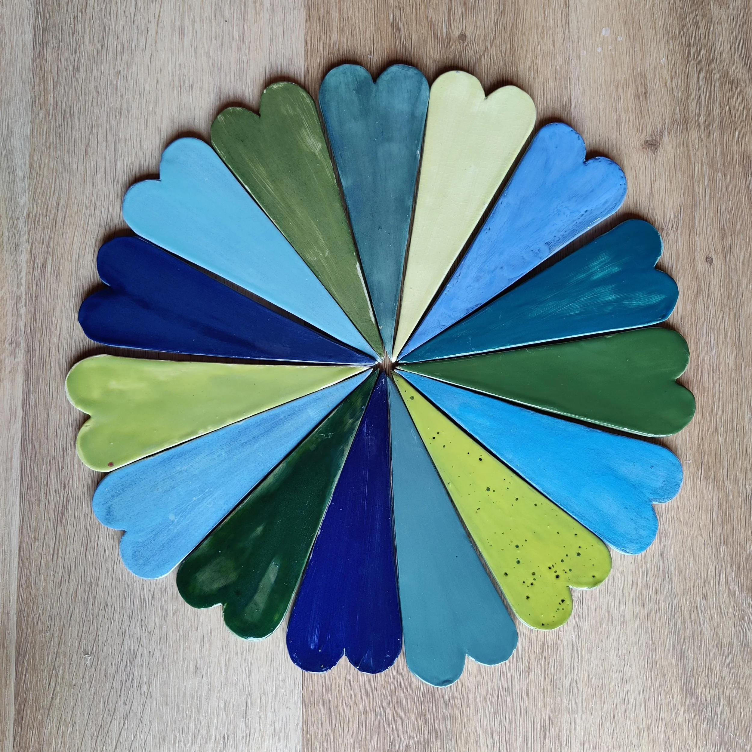 A circle made out of individual ceramic hearts with blue and green colour glazes.
