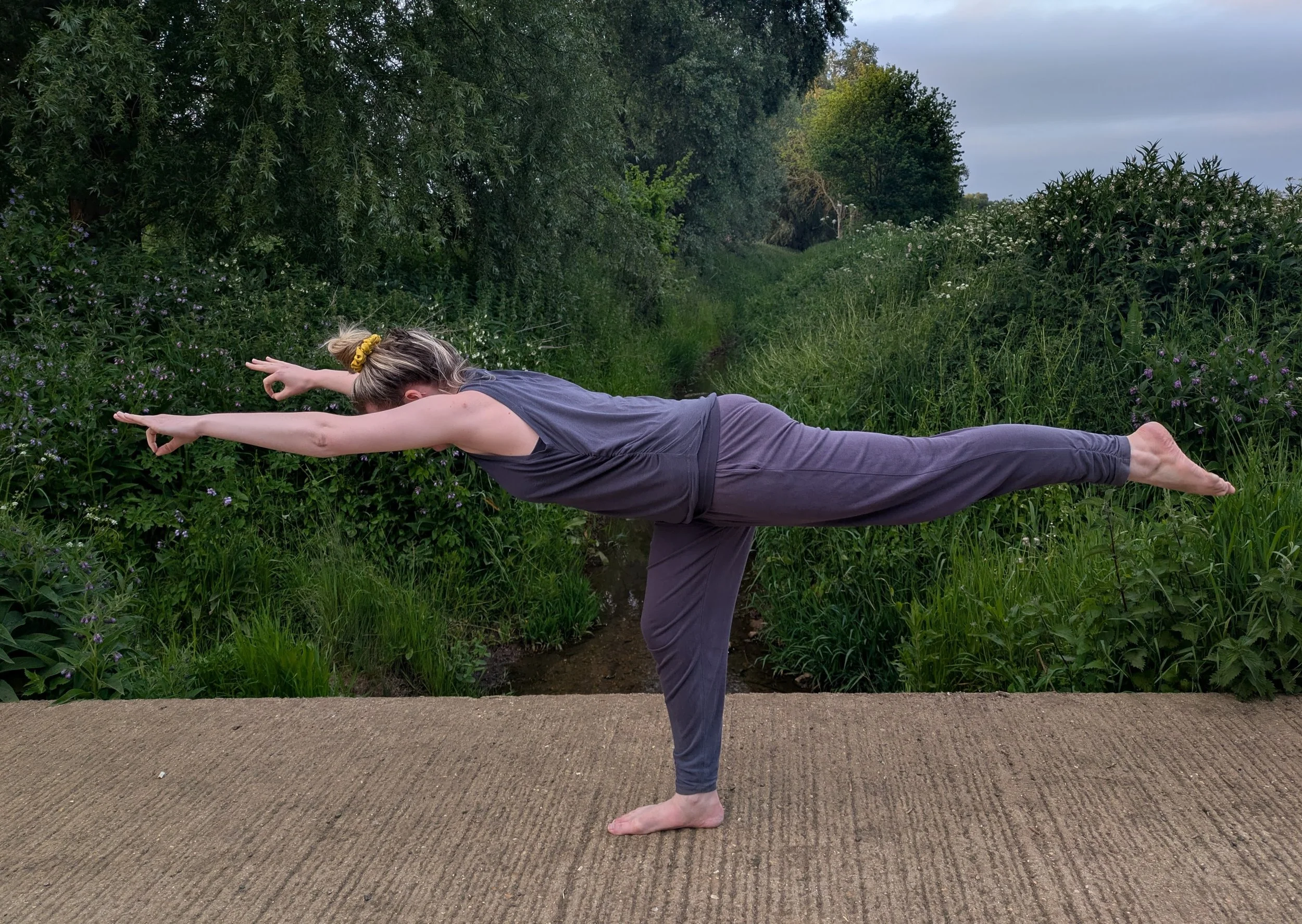Woman in a field in a warrior 3 yoga pose.