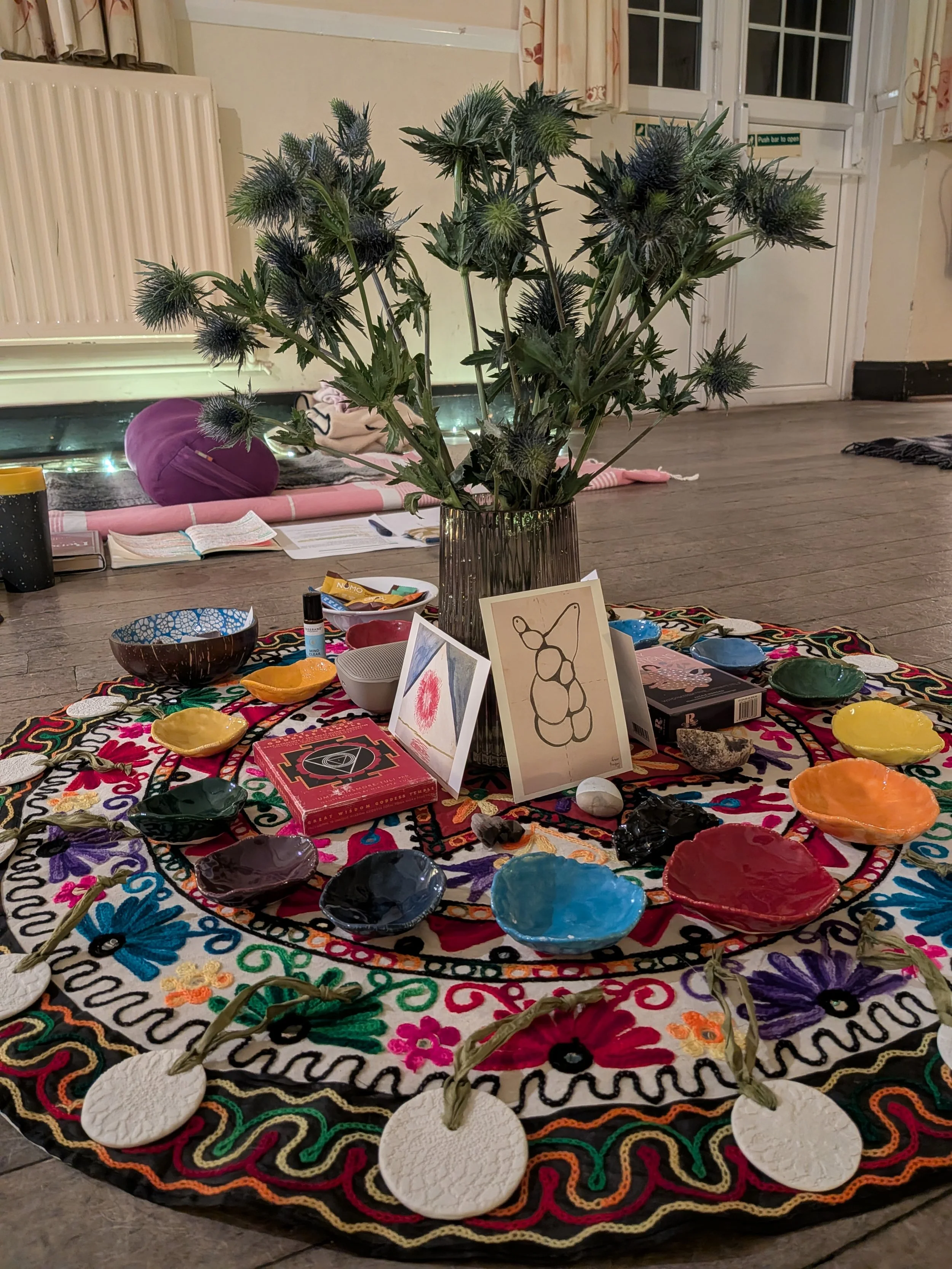 Flowers in a vase on a colourful circular piece of fabric, with small pieces of pottery placed on the mat.
