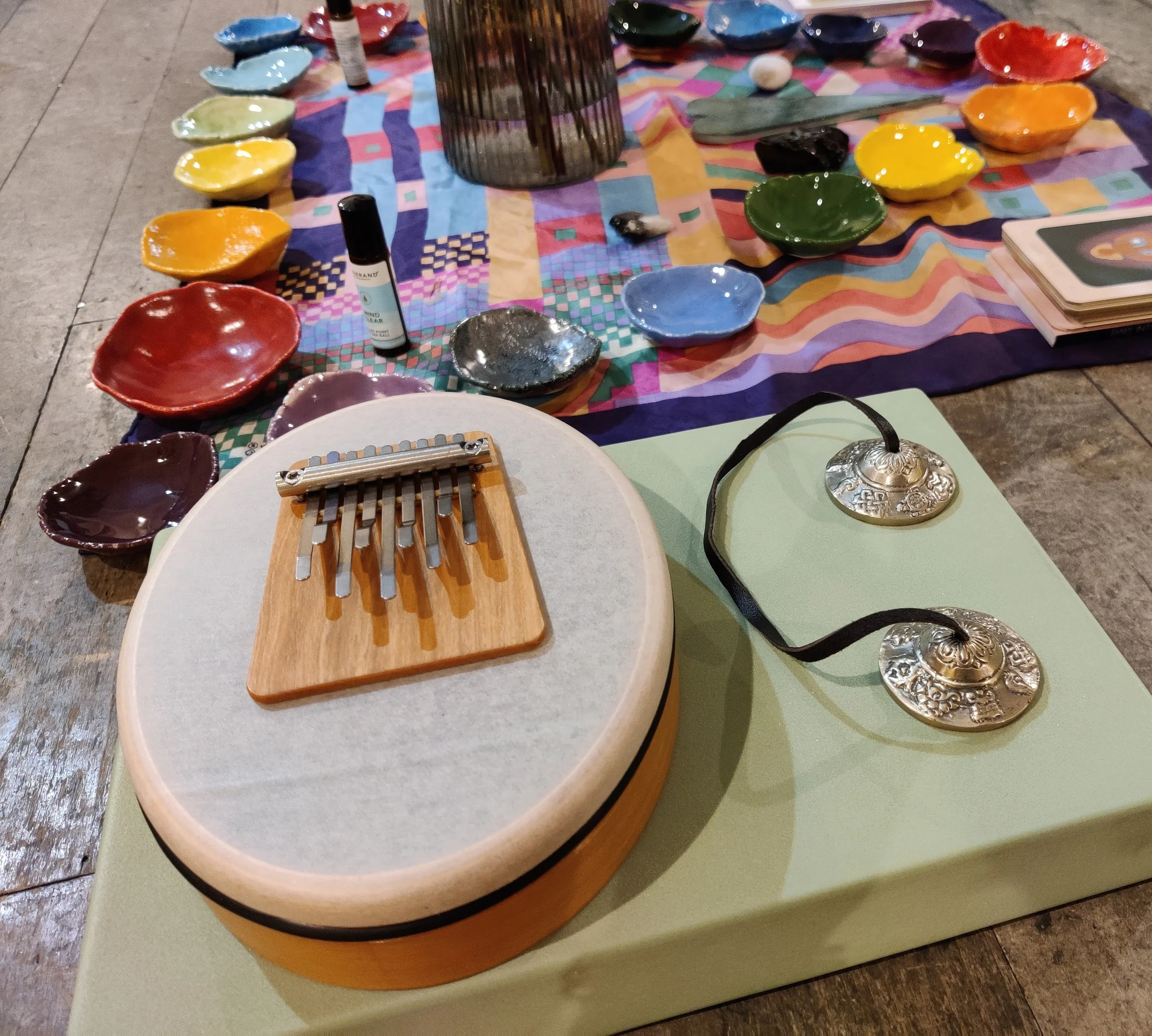 Small handheld musical instruments on a green block and colourful pottery on a piece of fabric.