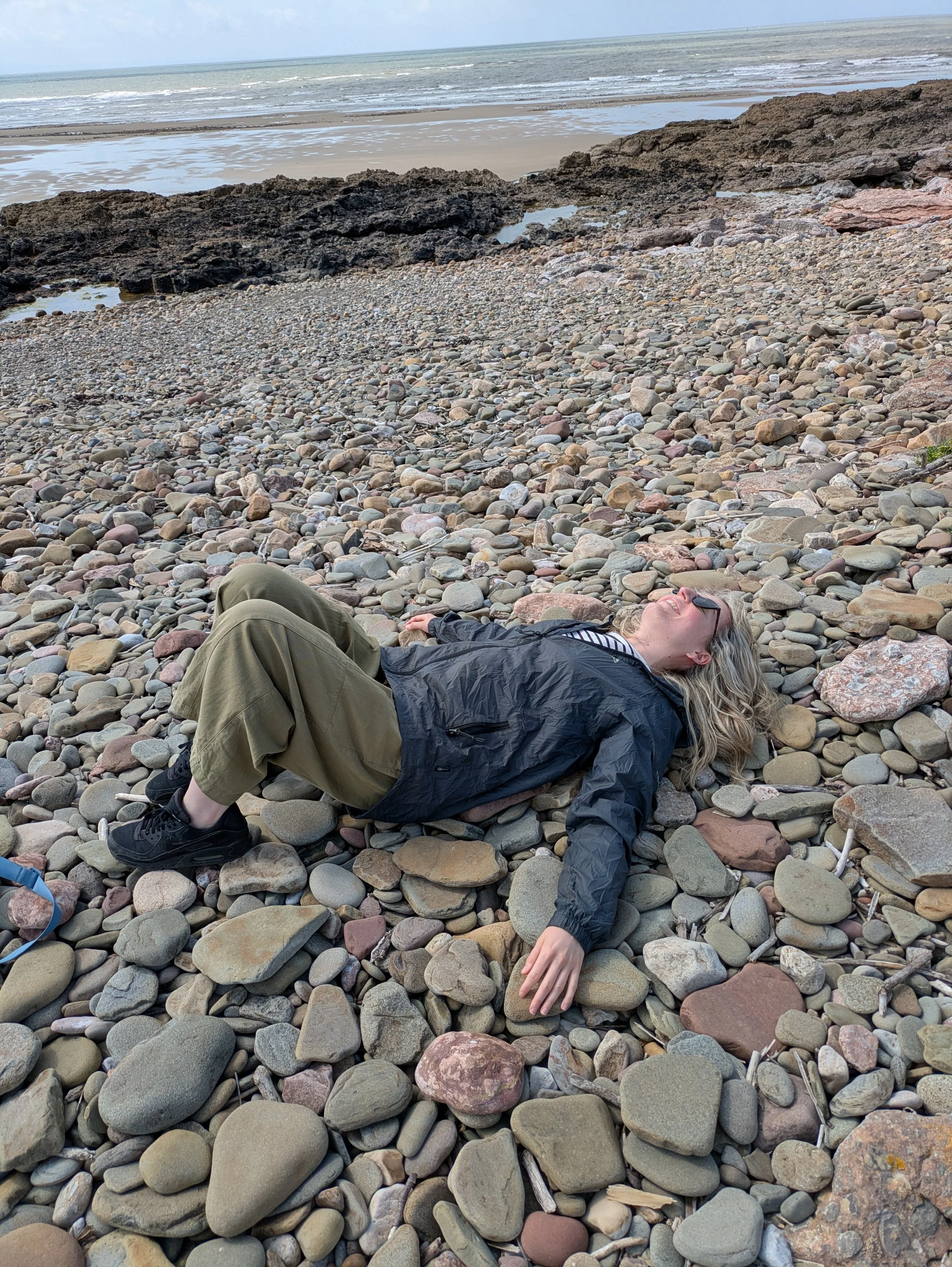 Woman laying on a stoney beach and smiling.