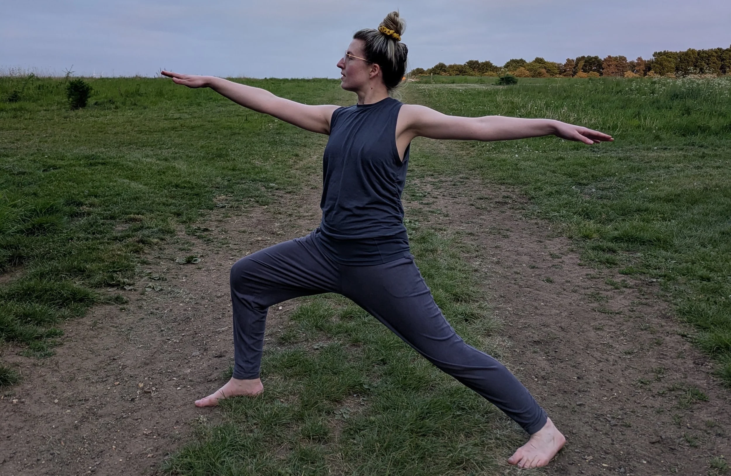 Woman in a field in a warrior 2 yoga pose.