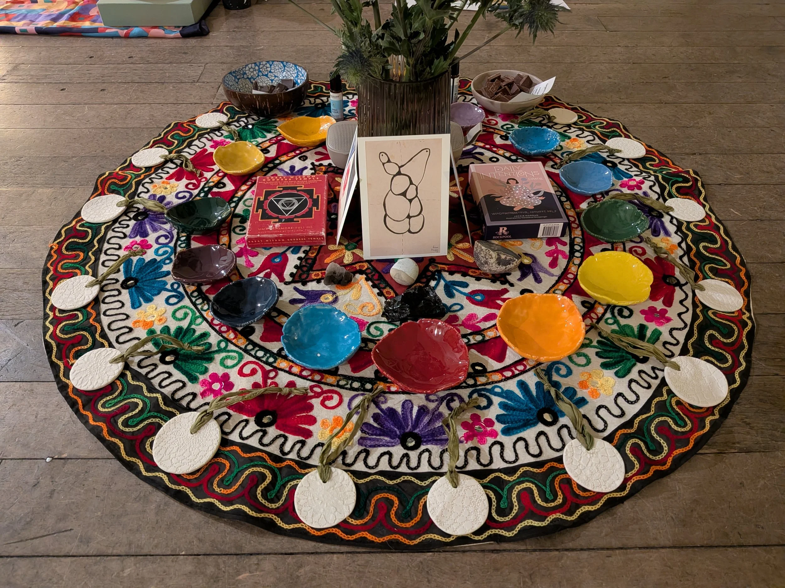 Colourful circular piece of fabric with various items displayed for a focus area, including small pieces of ceramics, tarot card decks, crystals and flowers, ready for the yoga nidra in Clifton, Bedfordshire.
