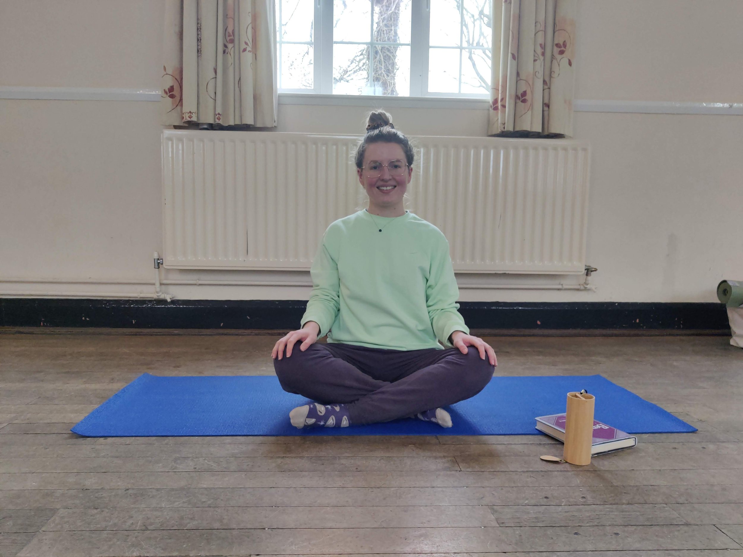 Woman sitting cross legged on a yoga mat and gently smiling.