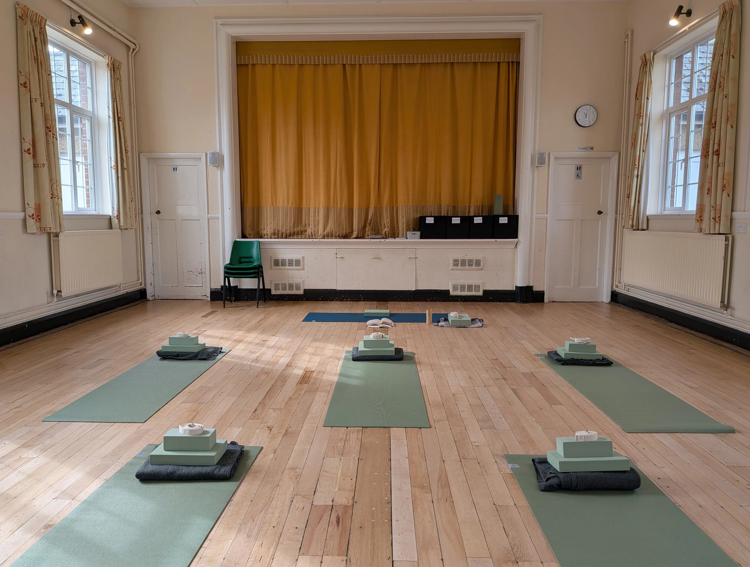 Green yoga mats with props and blanket in a bright and spacious hall with a wooden floor ready for a yoga class in Clifton, Bedfordshire