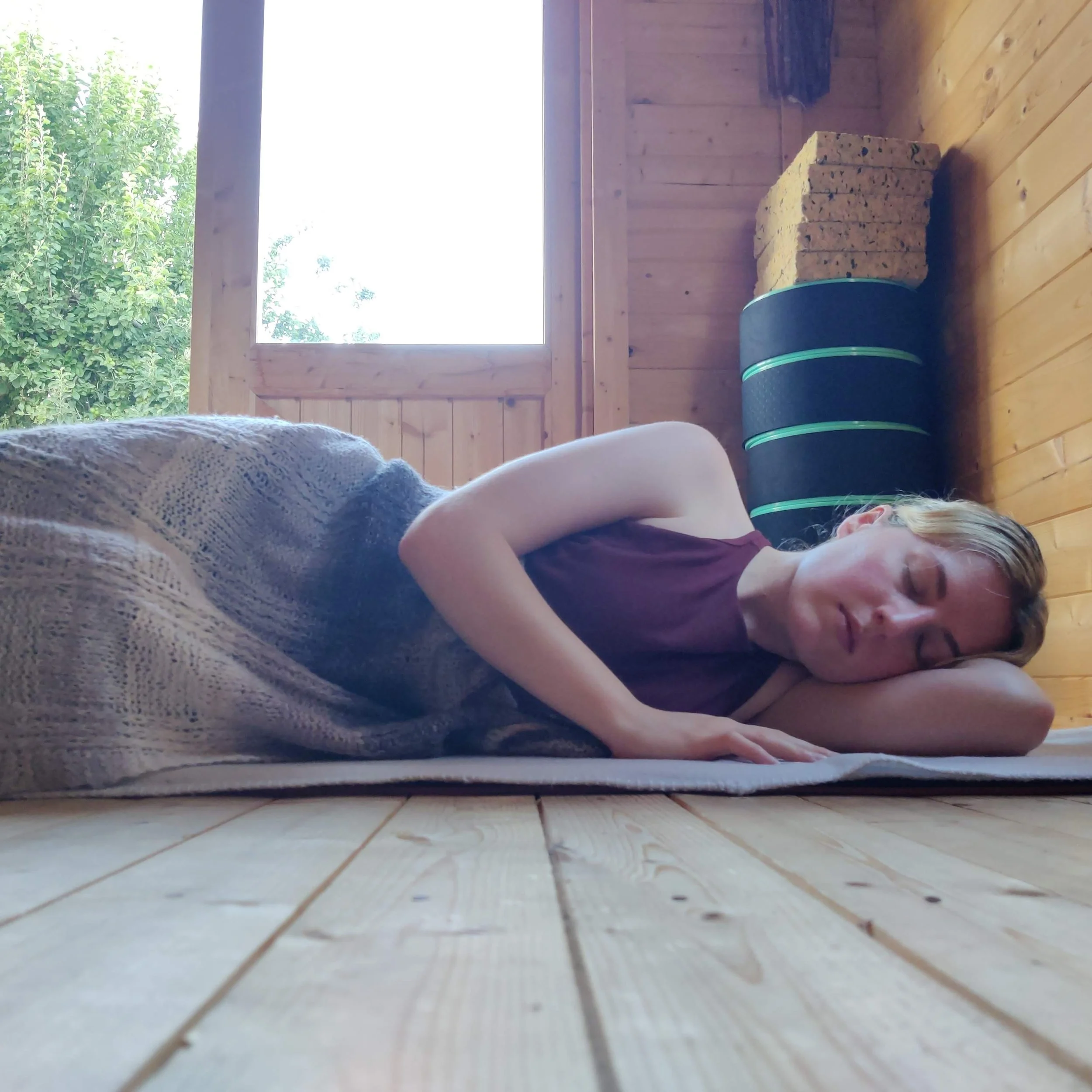 Woman laying on her side resting on a mat with a blanket over her.