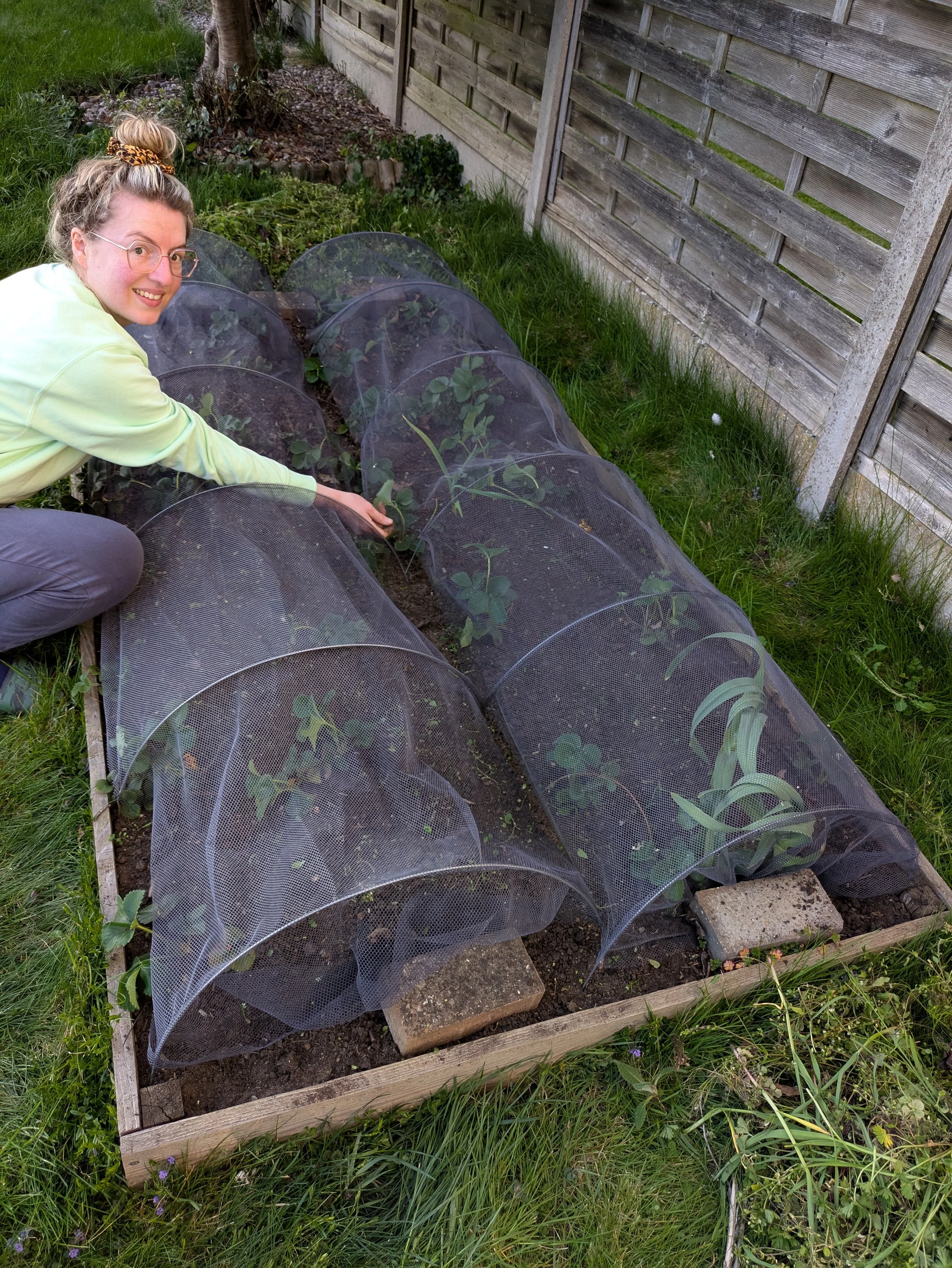 Woman in the garden crouching down to a vegetable patch and gently smiling.