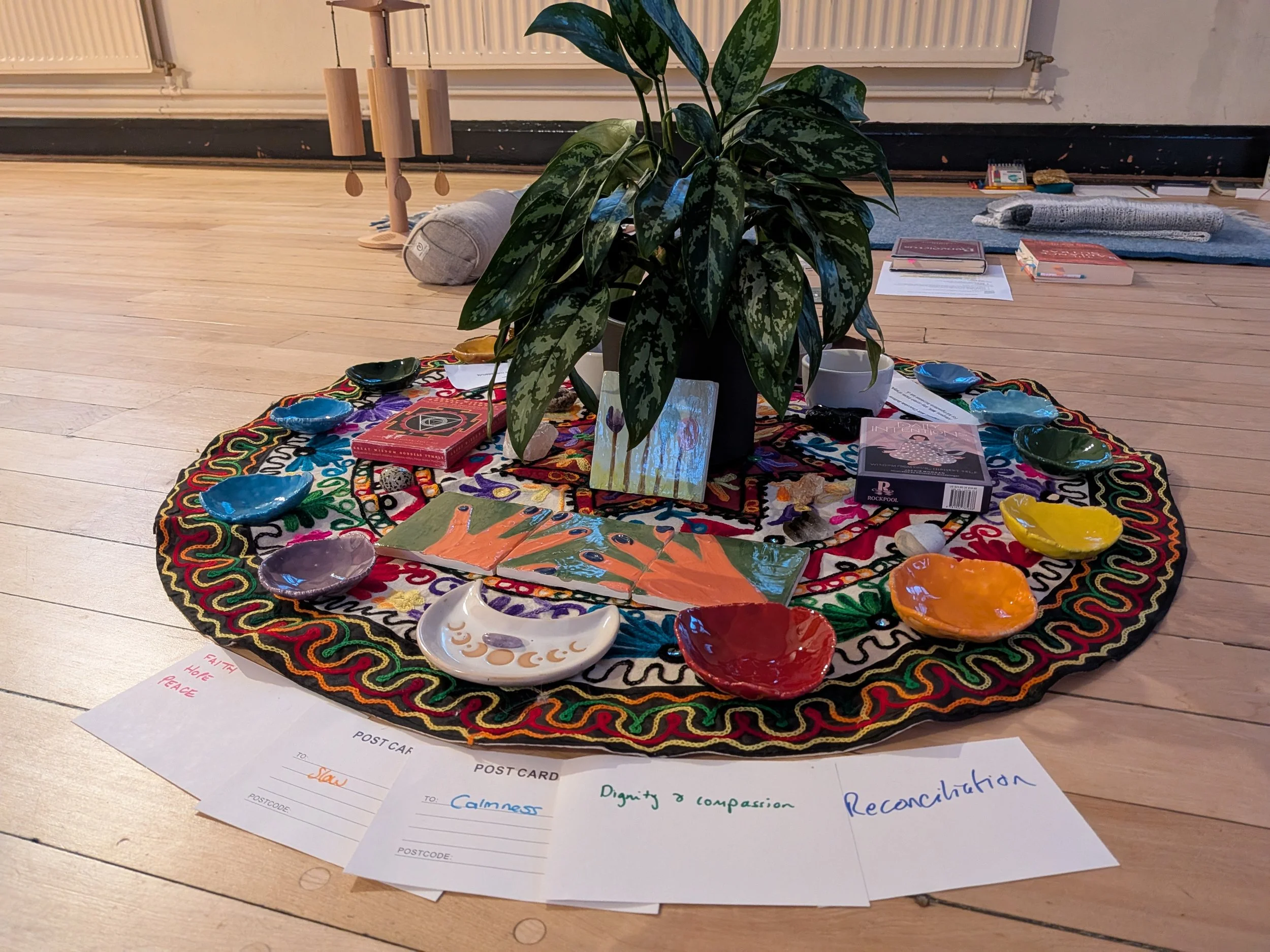 Colourful circular piece of fabric with various items displayed for a focus area, including small pieces of ceramics, tarot card decks, crystals and flowers, and pieces of white card, ready for the yoga nidra in Clifton, Bedfordshire