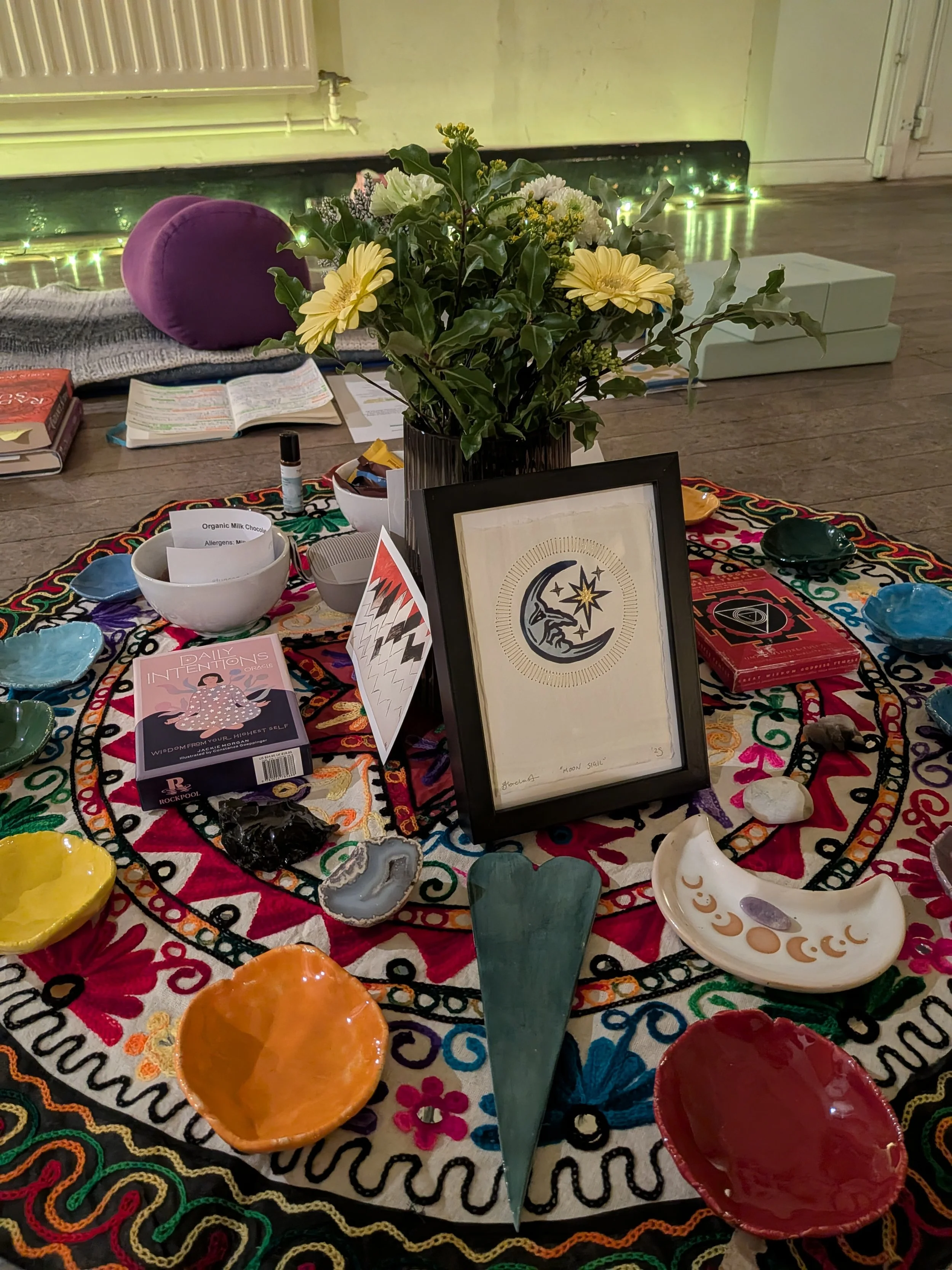 Colourful circular piece of fabric with various items displayed for a focus area, including small pieces of ceramics, tarot card decks, crystals and flowers, ready for the yoga nidra in Clifton, Bedfordshire.