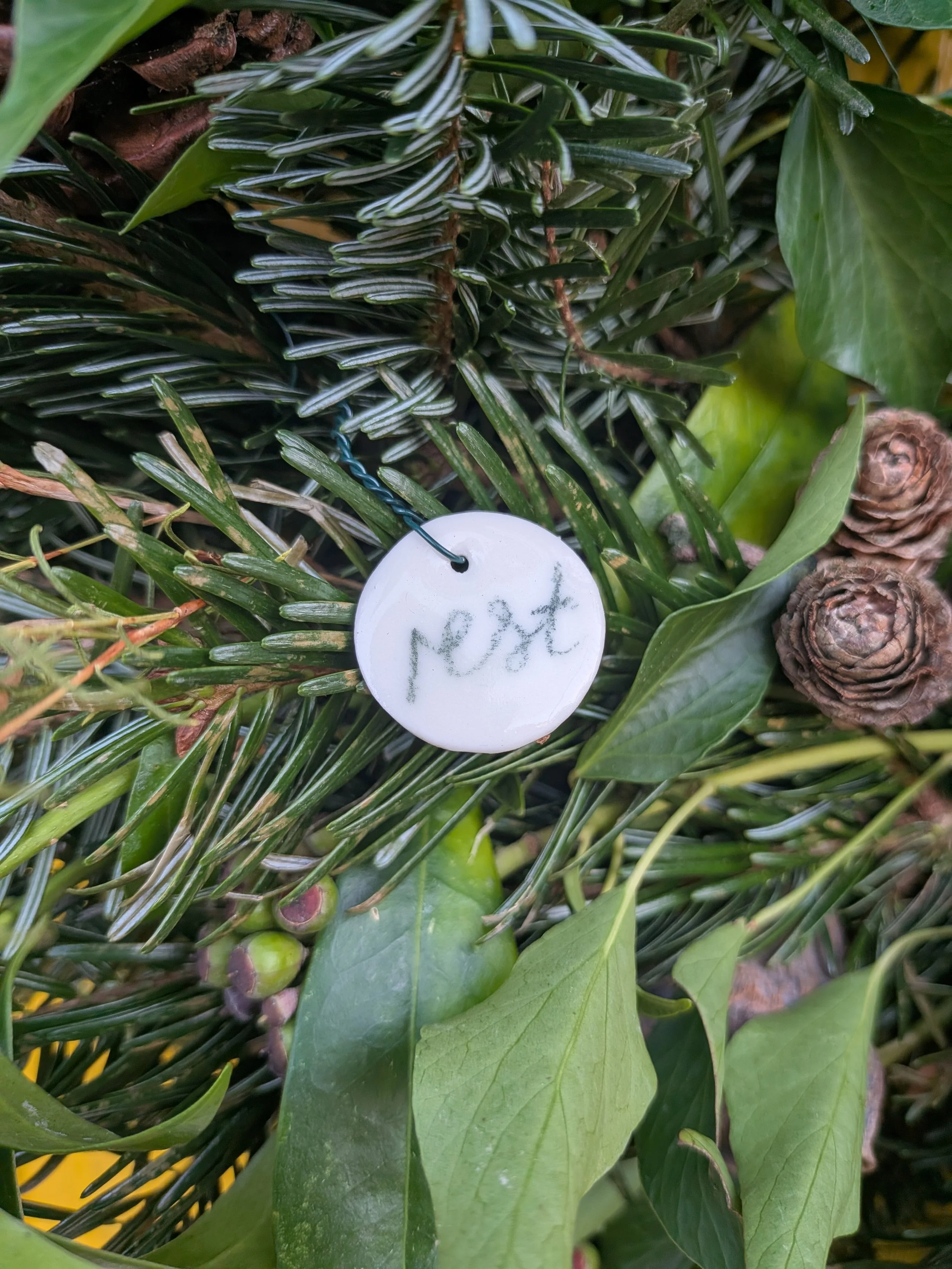 Close up of green foliage with a white ceramic circle attached to it with the word 'rest' handwritten on it.