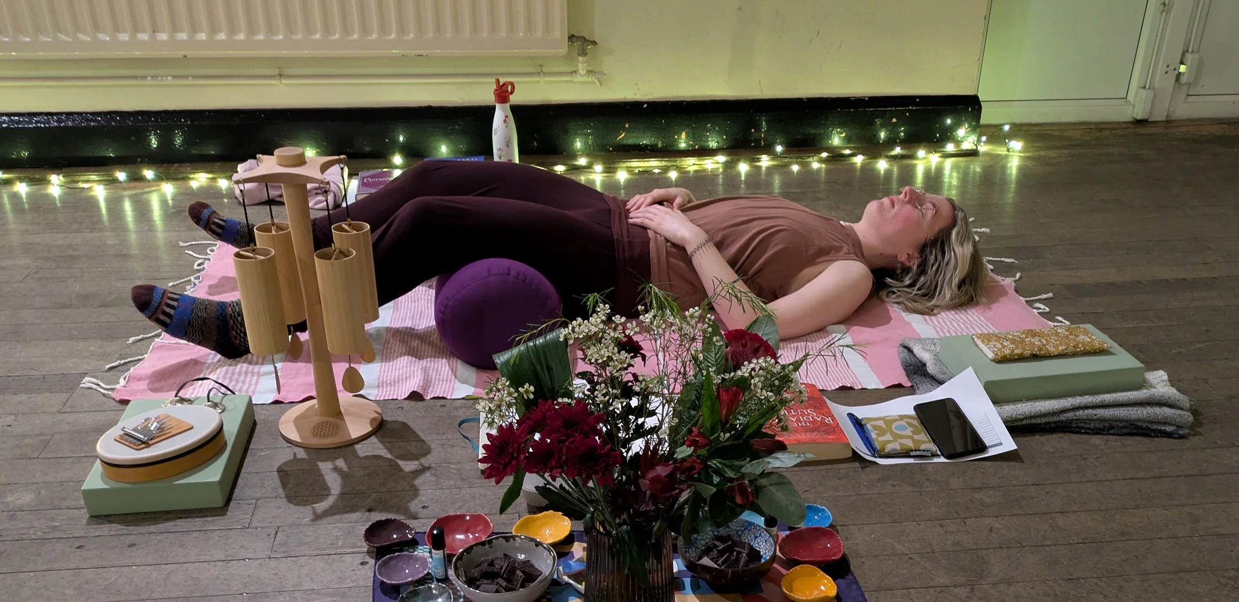 Woman laying on a yoga mat with hands on abdomen and bolster under knees