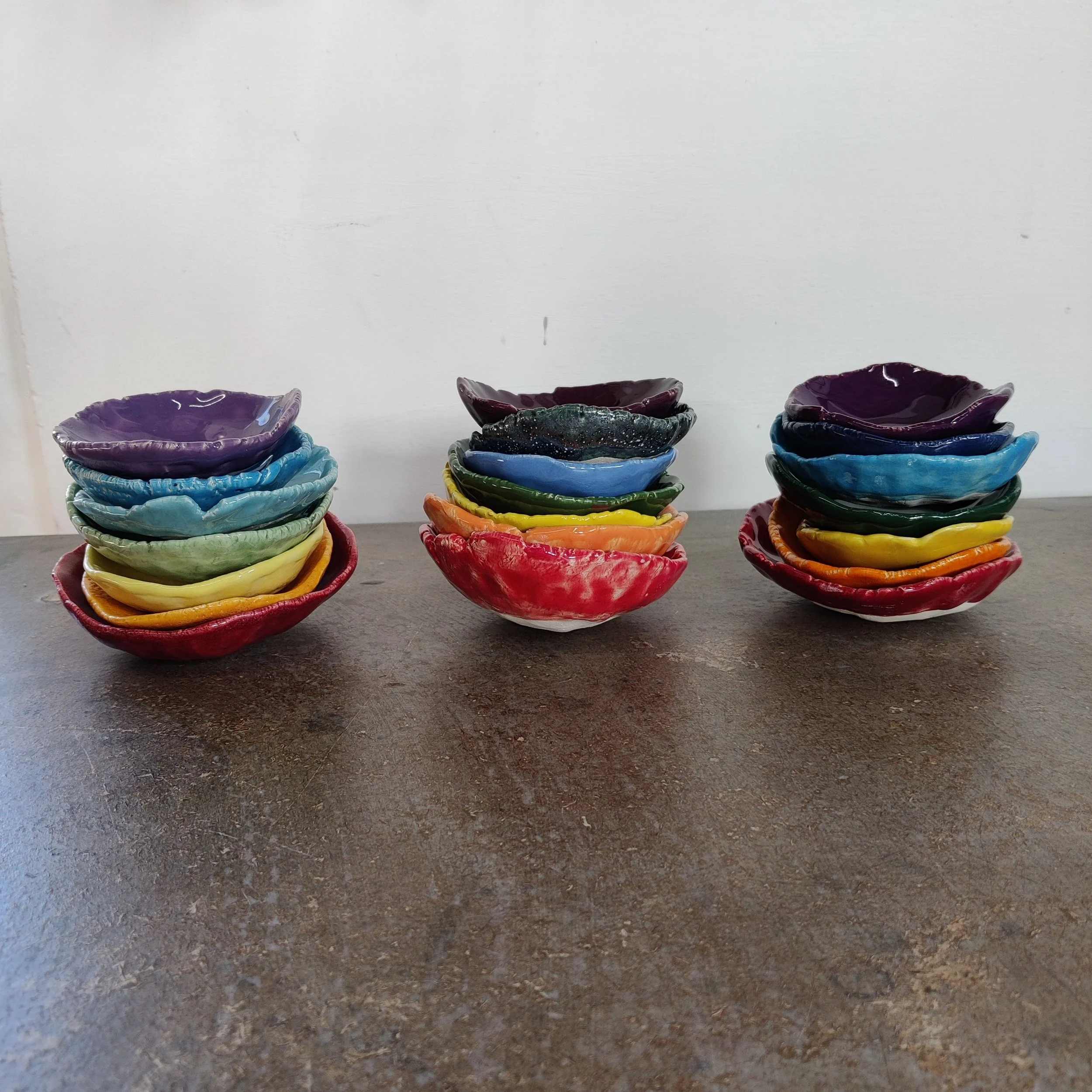 Three stacks of small pottery pots in different rainbow colours representing the seven chakras.