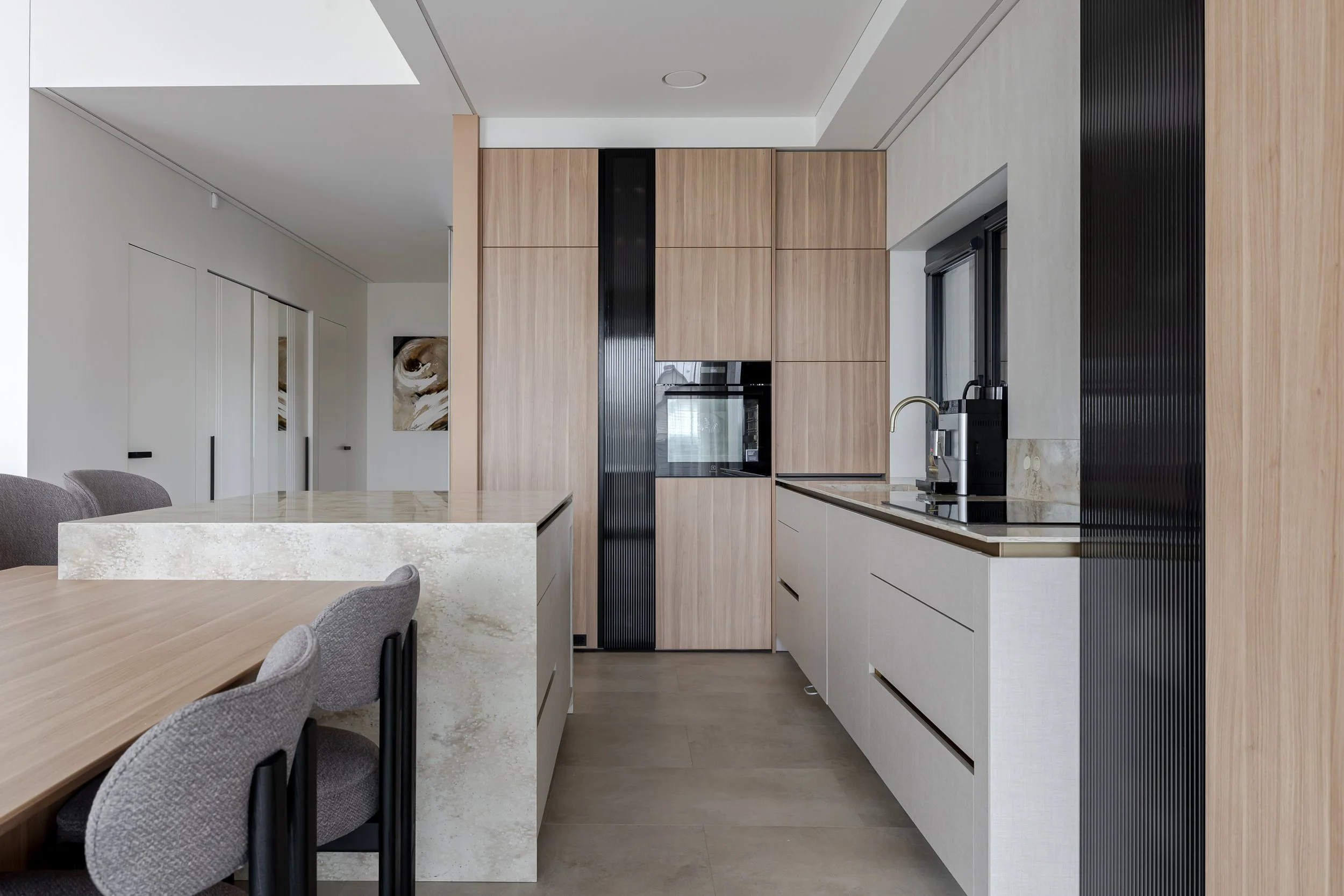 Modern kitchen with light wood and white cabinetry, black accents, and gray chairs.