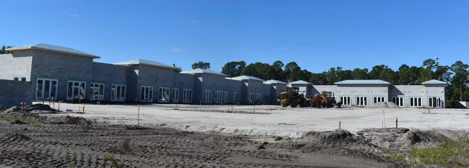 Under construction building with gray masonry walls, multiple glass doors, and construction equipment on site.