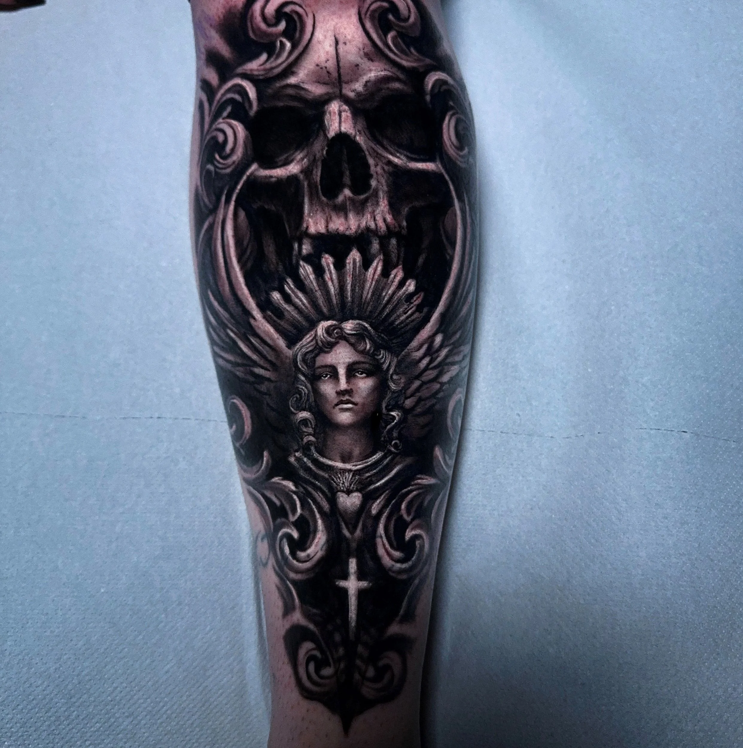 Dark realism tattoo of an angel and a skull done on a lower leg