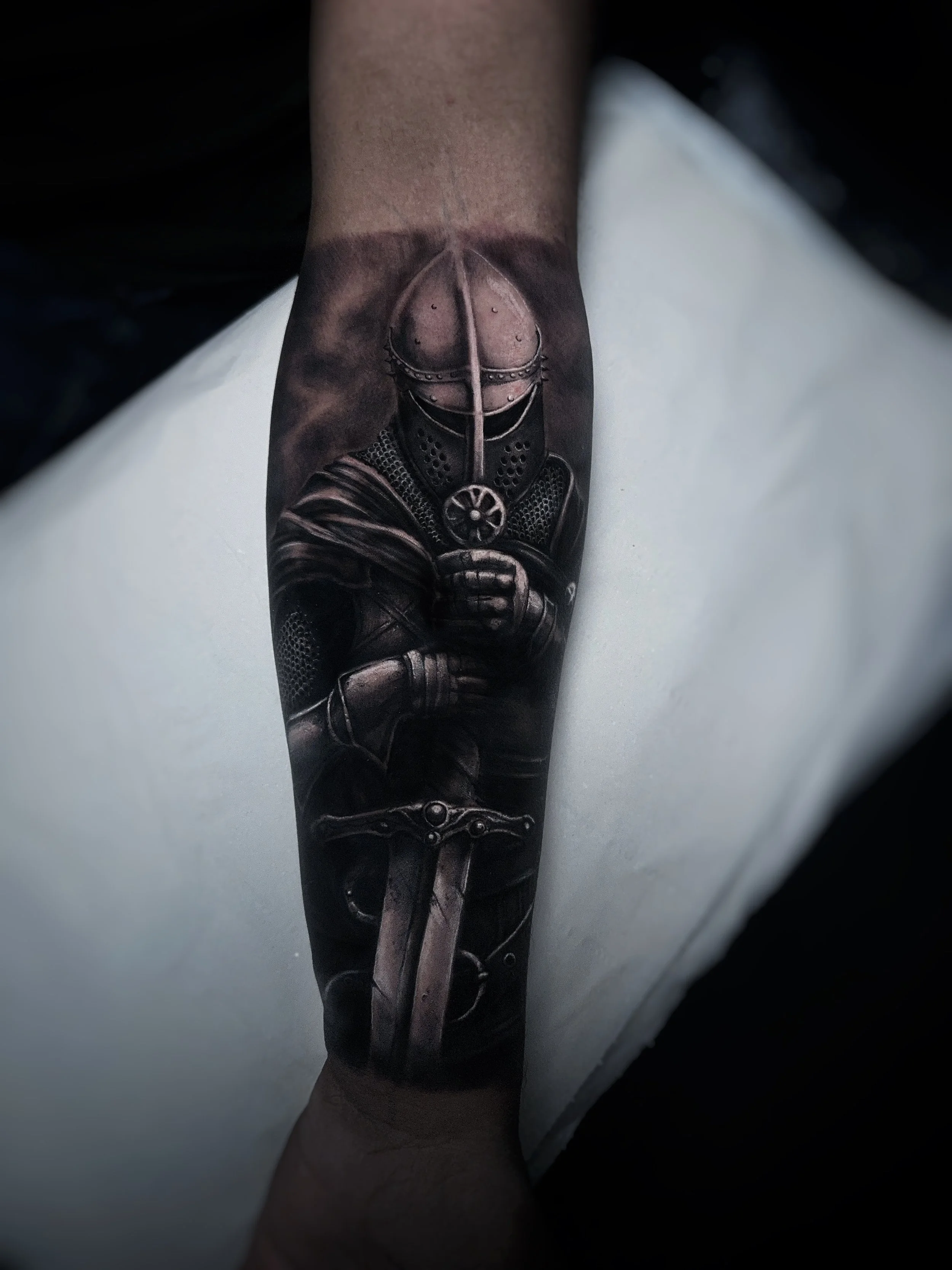 Black and Grey Unterarm Tattoo mit Rittermotiv, Schwert und atmosphärischem Hintergrund.