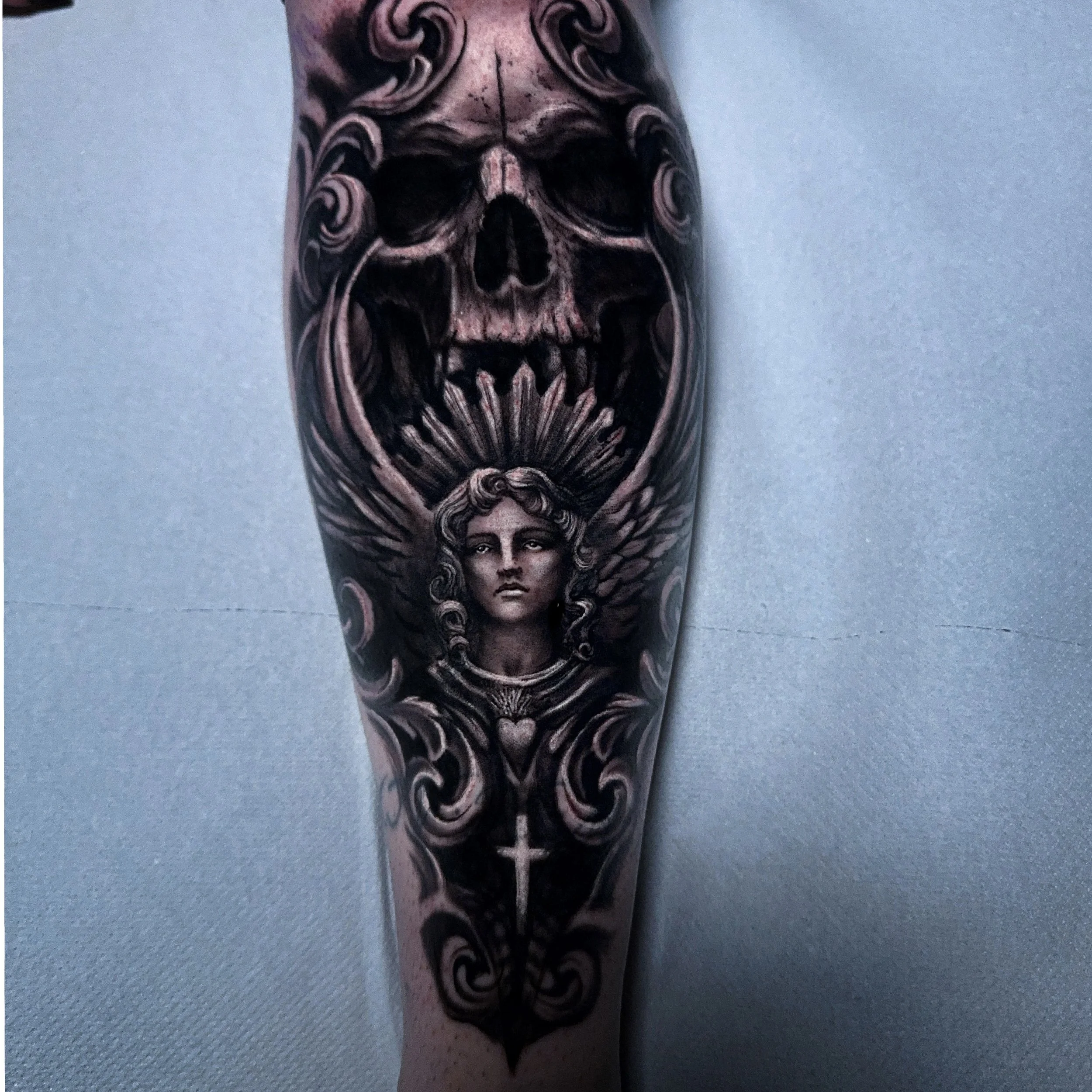 Dark realism tattoo of an angel and a skull done on a lower leg