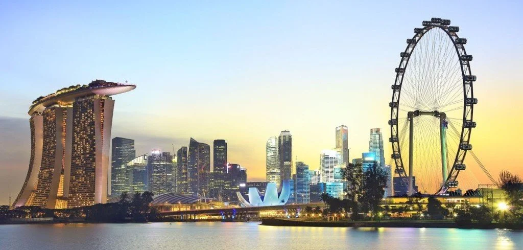 Singapore skyline at sunset featuring Marina Bay Sands hotel and Ferris wheel.