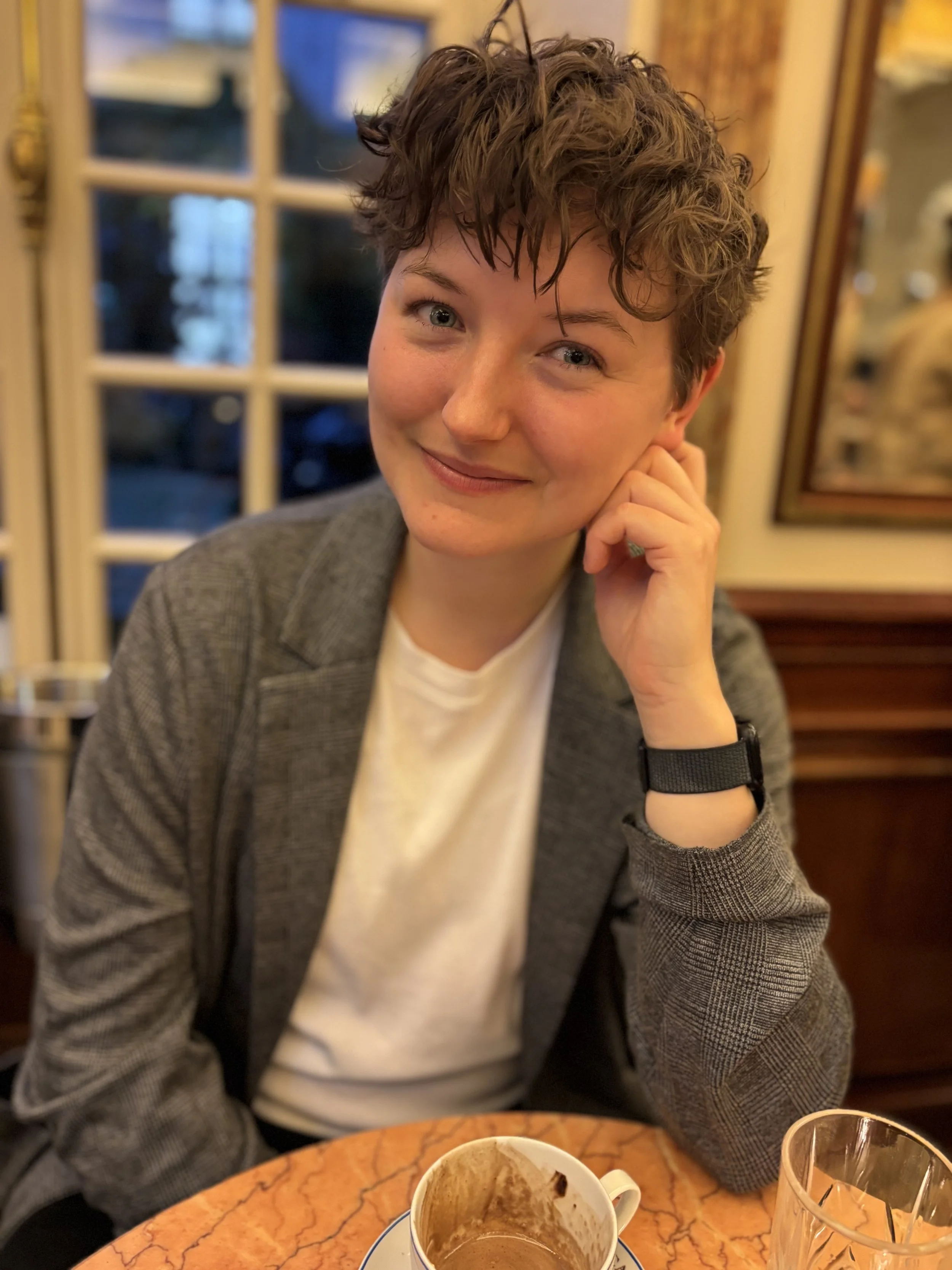 Young woman with short hair in a grey blazer looking at camera for profile photo in a cafe