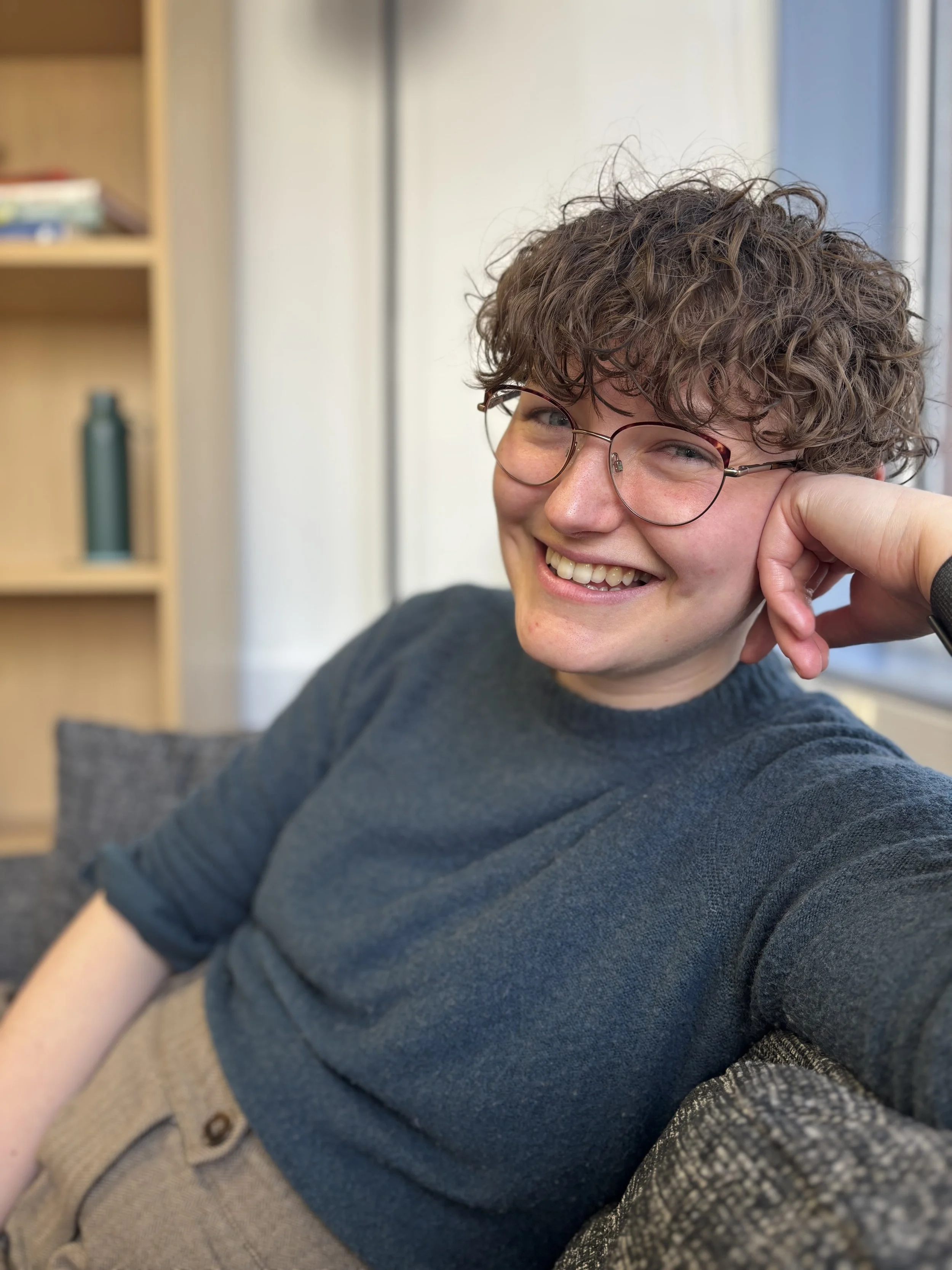 person in blue top and glasses sitting on sofa