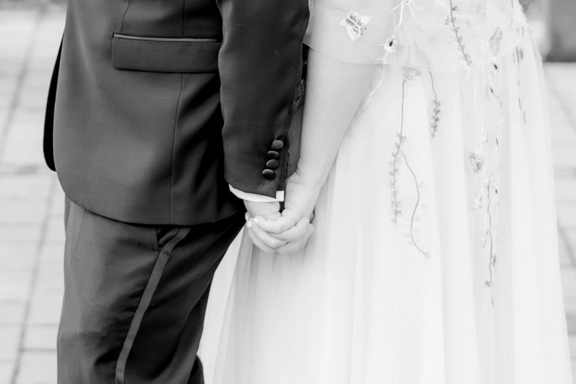 Close-up of a couple holding hands during a wedding ceremony, with the bride in a floral dress and the groom in a dark suit.