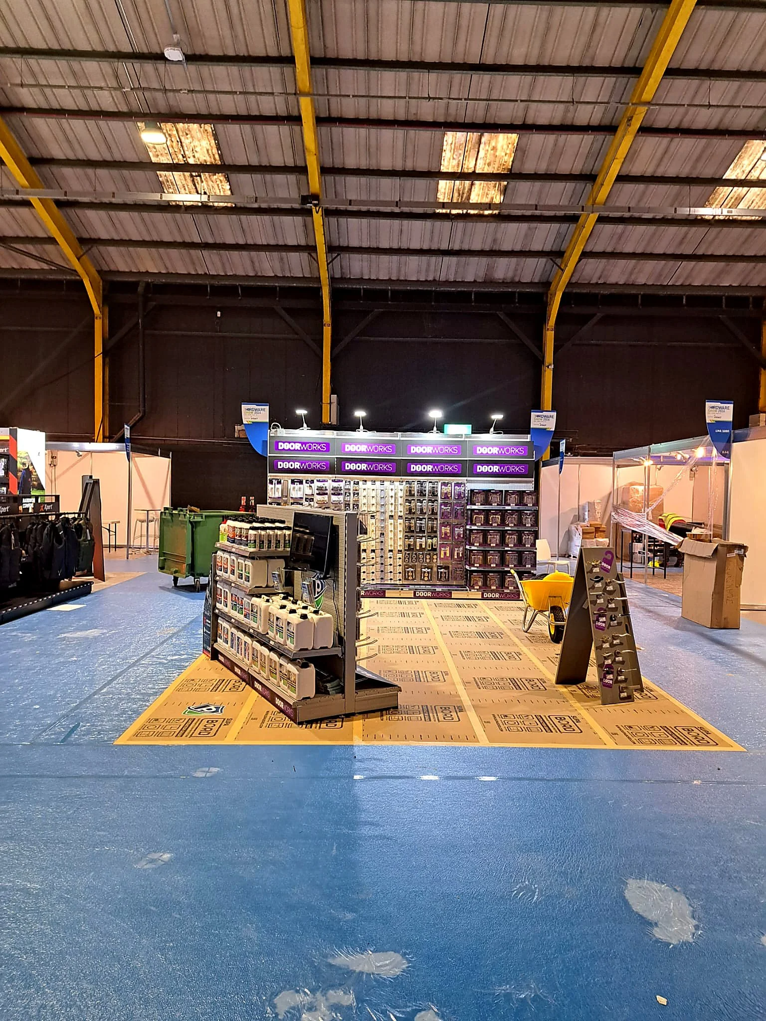 Inside of an unfinished warehouse or store with a blue plastic covered floor, showing a display of hardware tools, doors, and other building supplies.