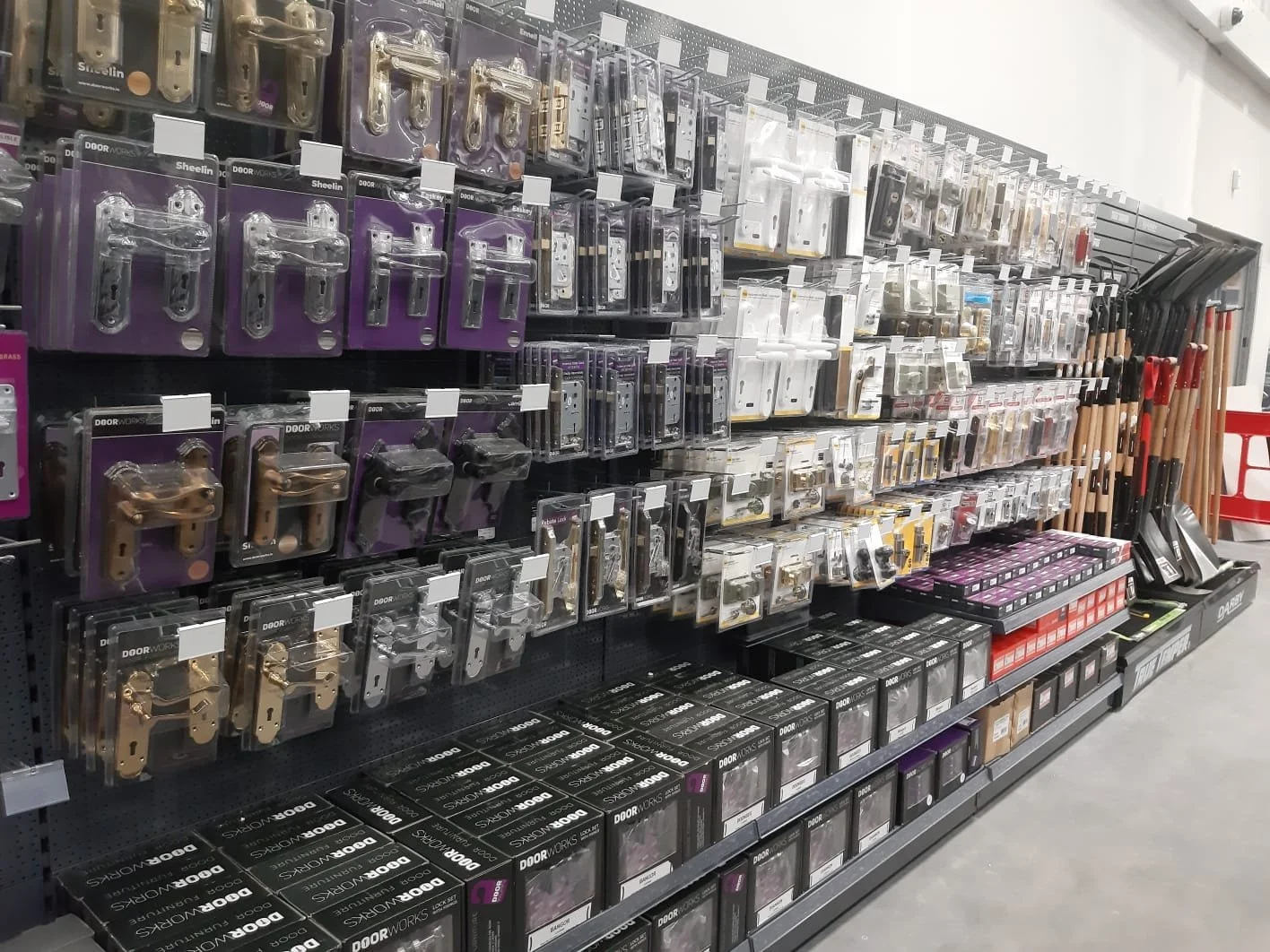 Retail store aisle displays door hardware such as locks, handles, and latches, organized on hooks and shelves.