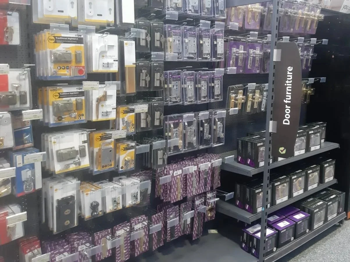 Interior view of a store aisle with door hardware and locks displayed on shelves, organized by type and color.