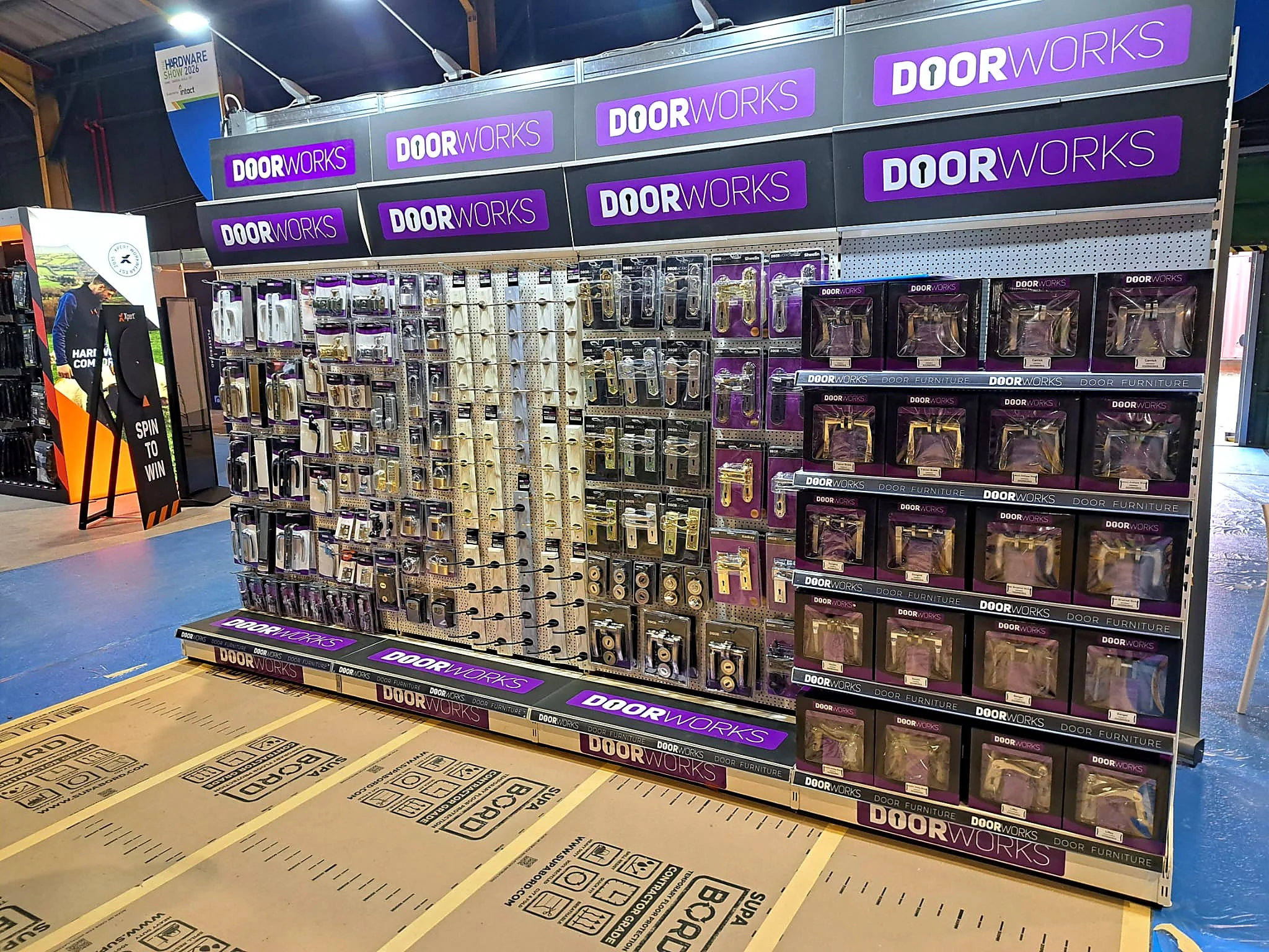 A display of door hardware such as handles, locks, and hinges at a hardware store, with purple DoorWorks branding signs above the items.