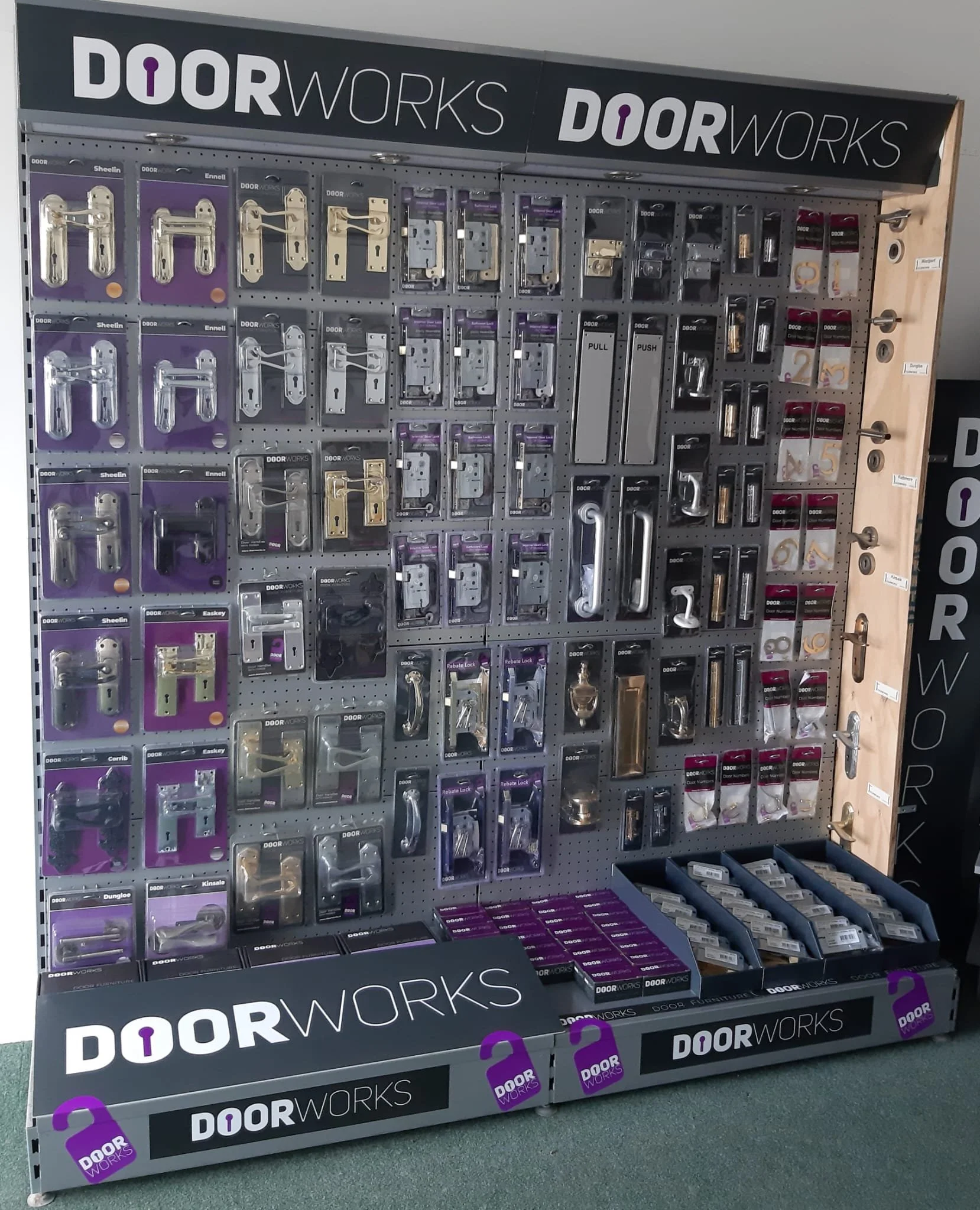 Display of various door hardware and locks on a retail wall in a hardware store, branded with DOORWORKS logo.