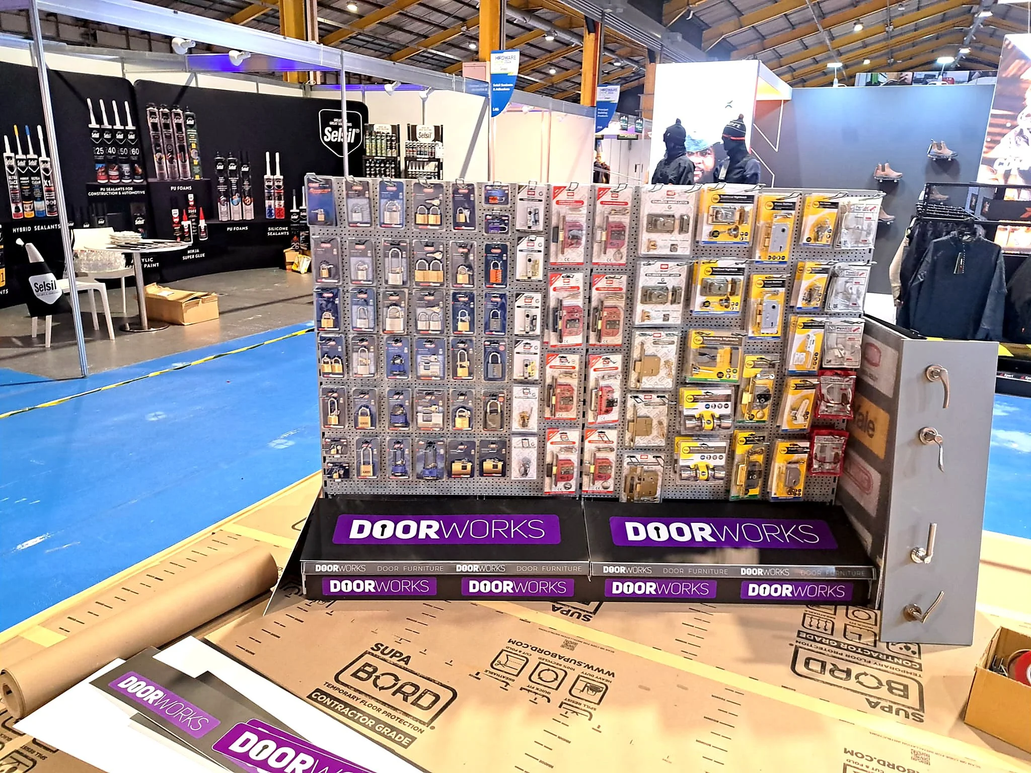 A display booth at a trade show showcasing various door hardware and accessories, with a black and purple "Doorworks" branding at the front.