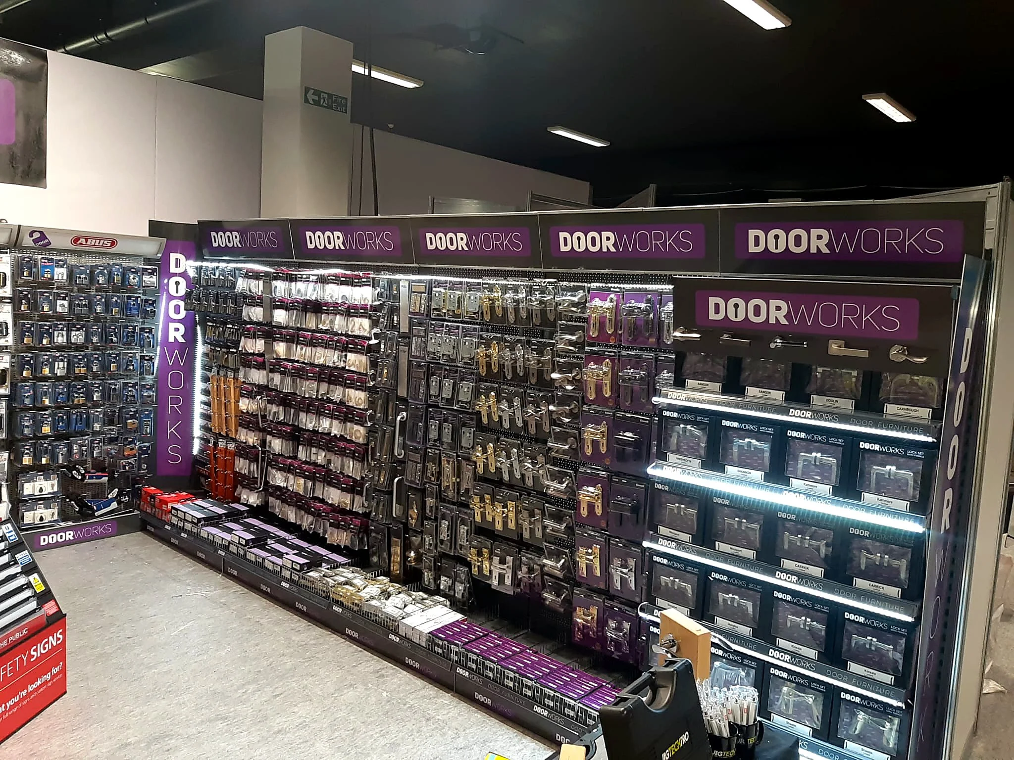 Store aisle displaying door locks and hardware accessories with purple 'DoorWorks' signage overhead.