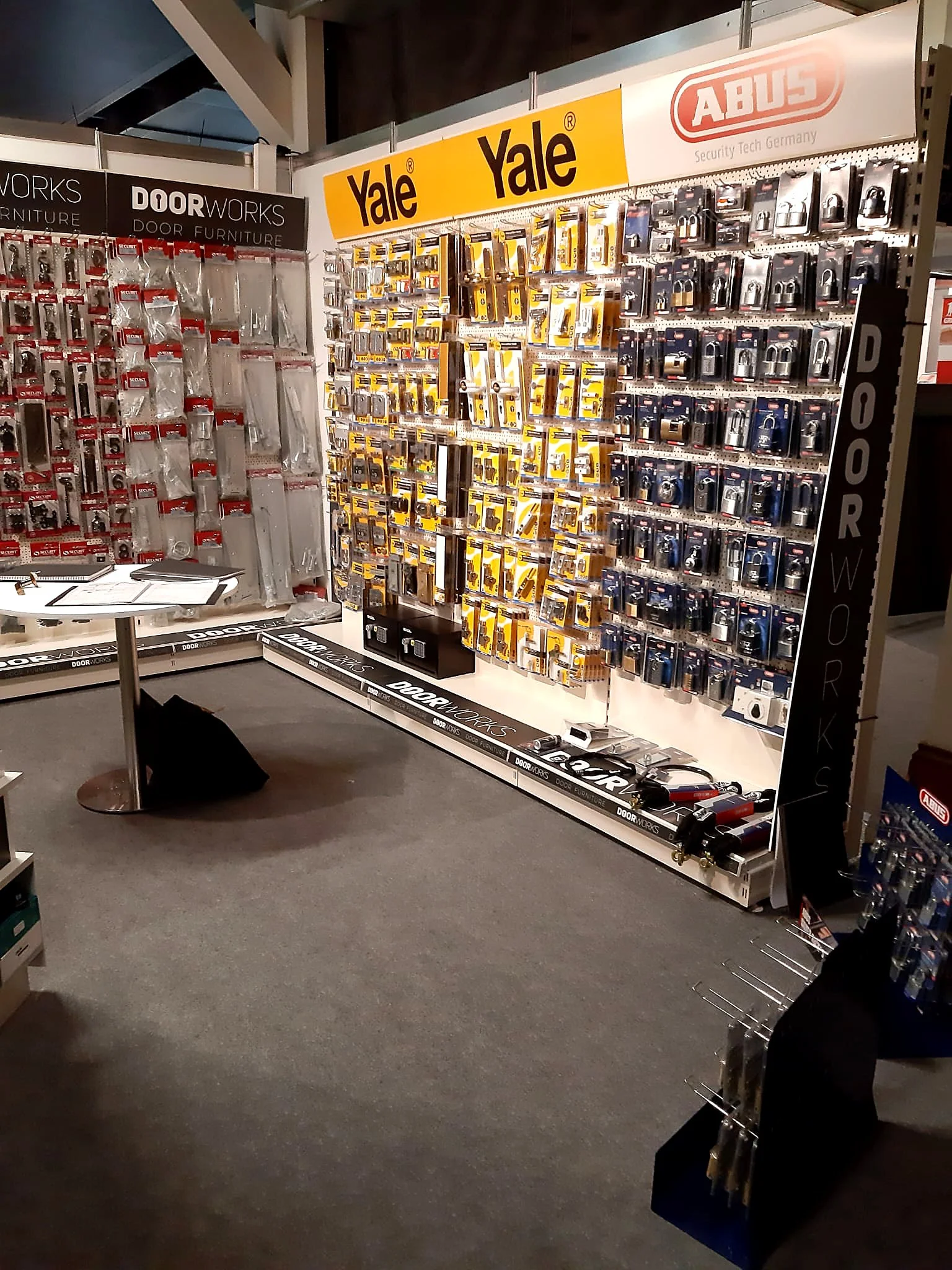 Display of door hardware and locks at a retail store, with brand signs for Yale and Abus, including padlocks and door accessories.