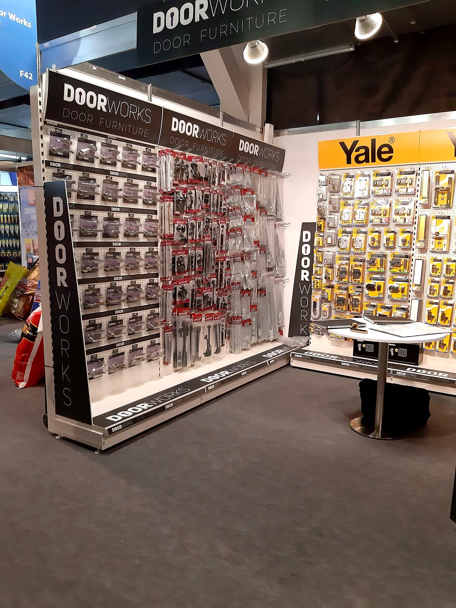 Display shelf in a store showing door hardware and furniture accessories with signage reading 'Door Works Door Furniture' and a yellow 'Yale' branded display.