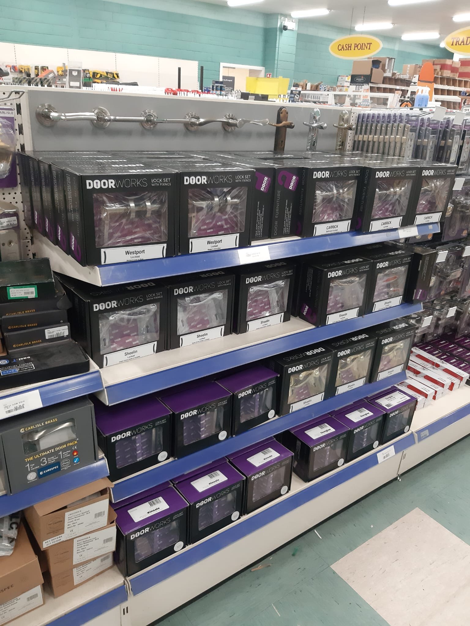 Store shelf displaying various door lock sets in black and purple boxes, with some metal door hardware parts visible above the boxes.