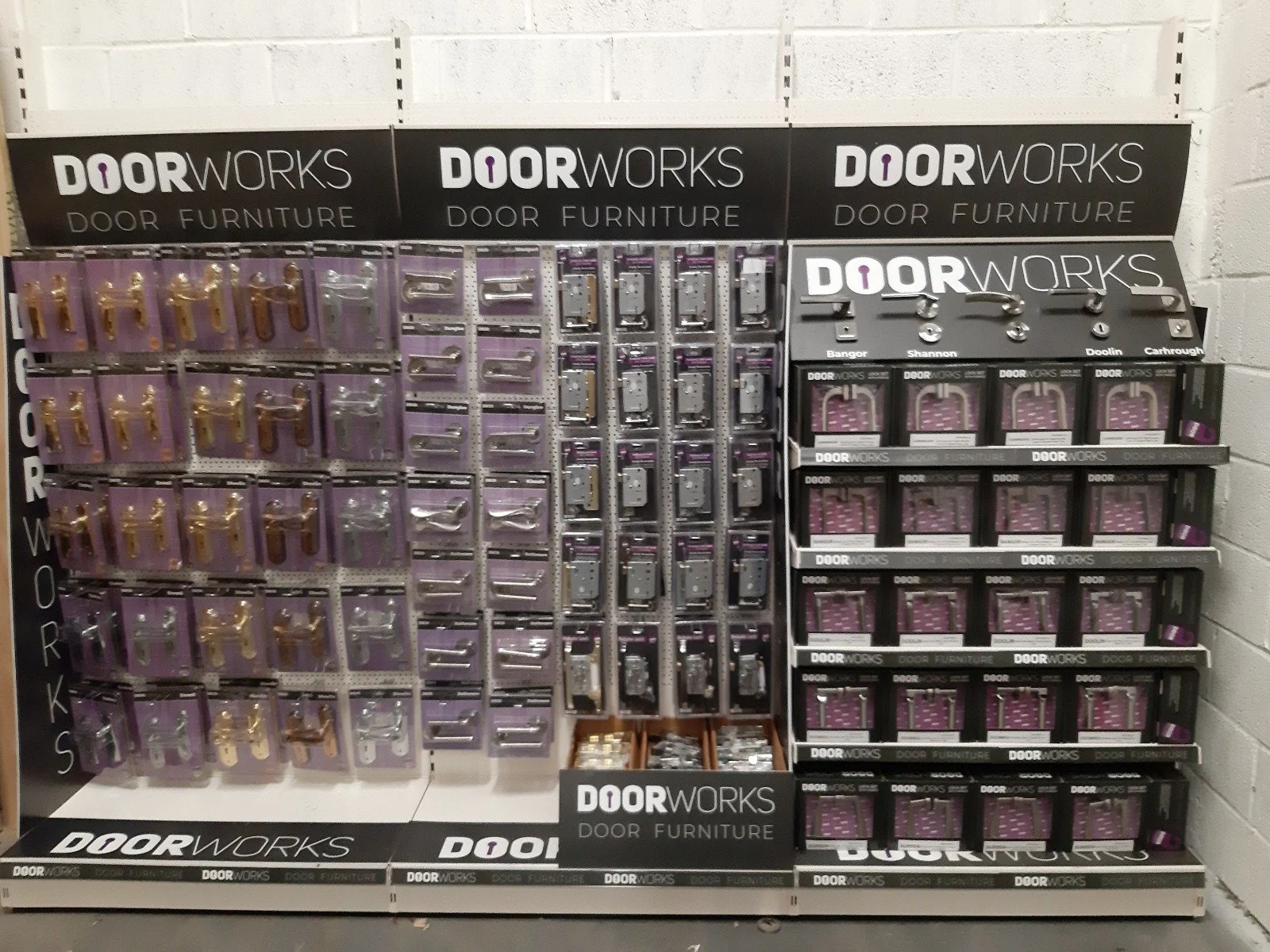 Display of door hardware and accessories at a Door Works store, including door knobs, handles, and locks in packaging on shelves.