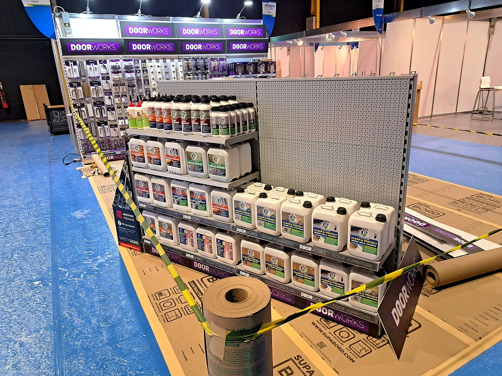 Display of cleaning products including bottles of cleaning solution at a hardware store, with signage for door hardware and a section labeled 'Doorworks' in the background.