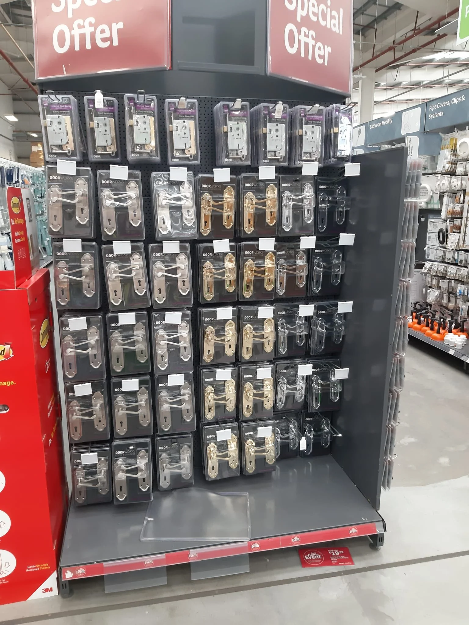 Display of various door locks and handles in a hardware store aisle, with red and black shelving and signage indicating a special offer.