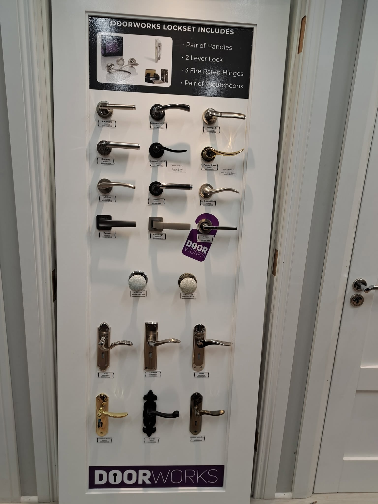 Display of various door handles and locks on a white board with a sign that reads 'Doorworks Lockset Includes.'