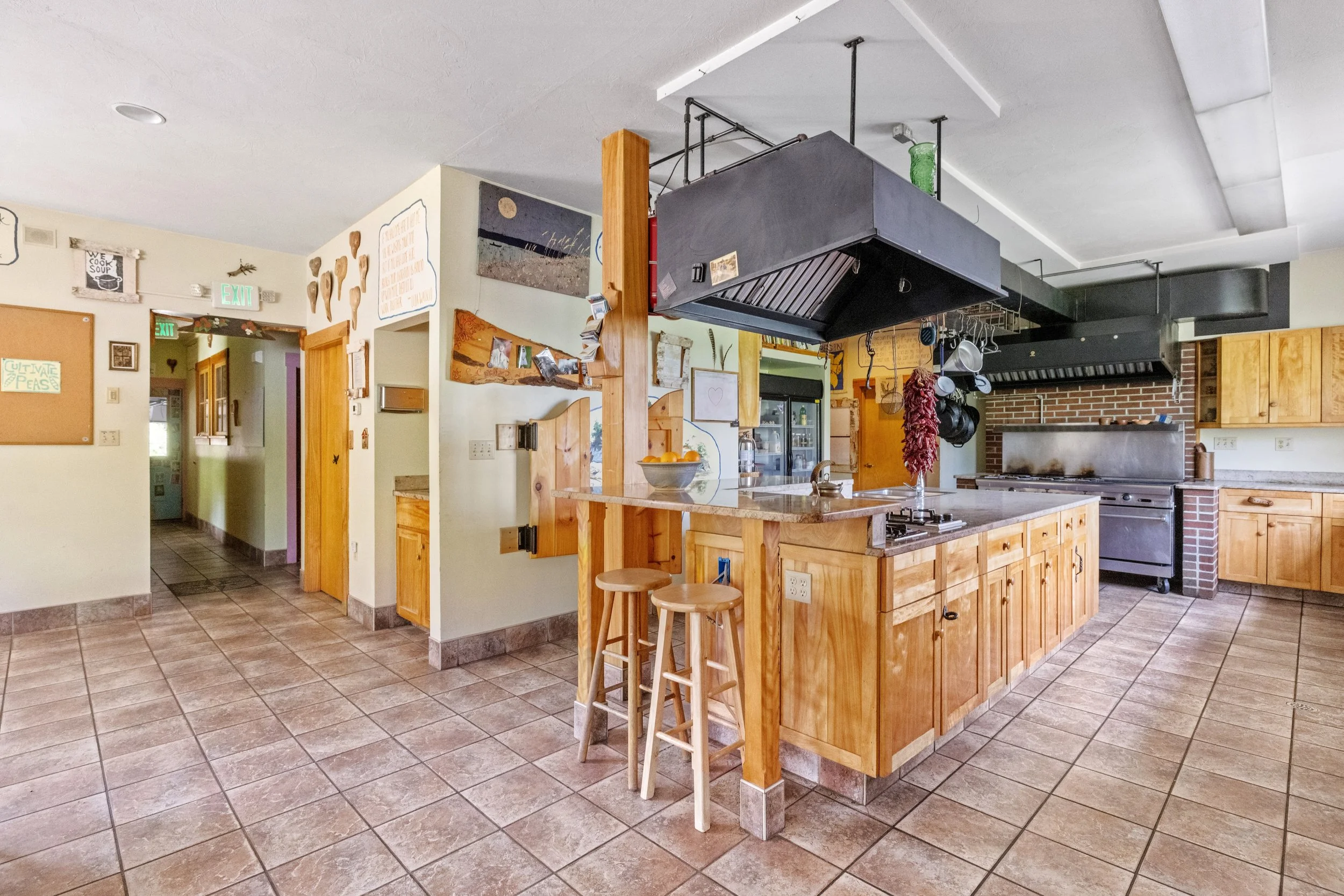A spacious kitchen with wooden cabinets, a large island, a brick wall with a stove, and hanging pots and pans.