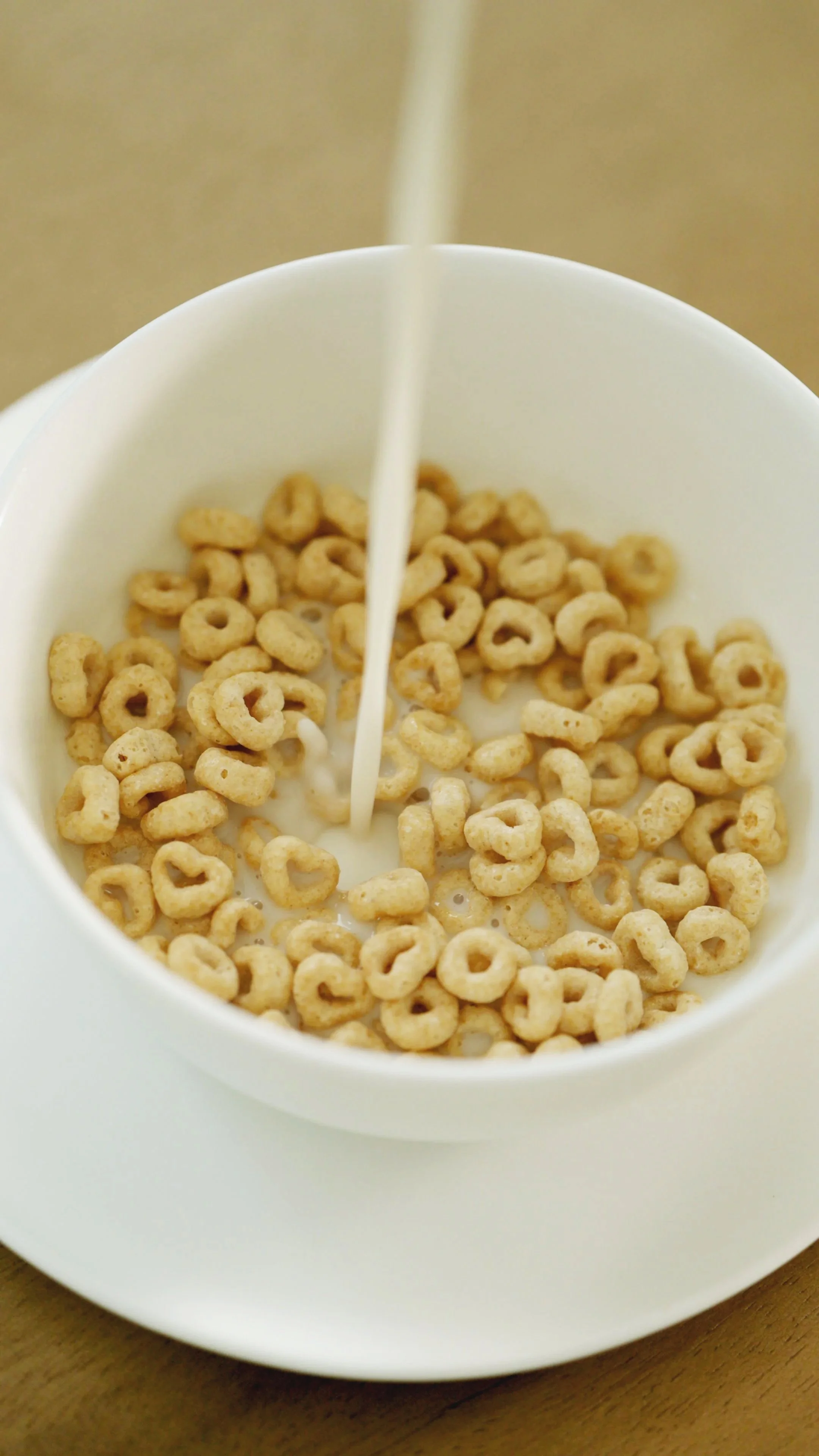 A white mug with cereal and milk, with milk pouring into it.