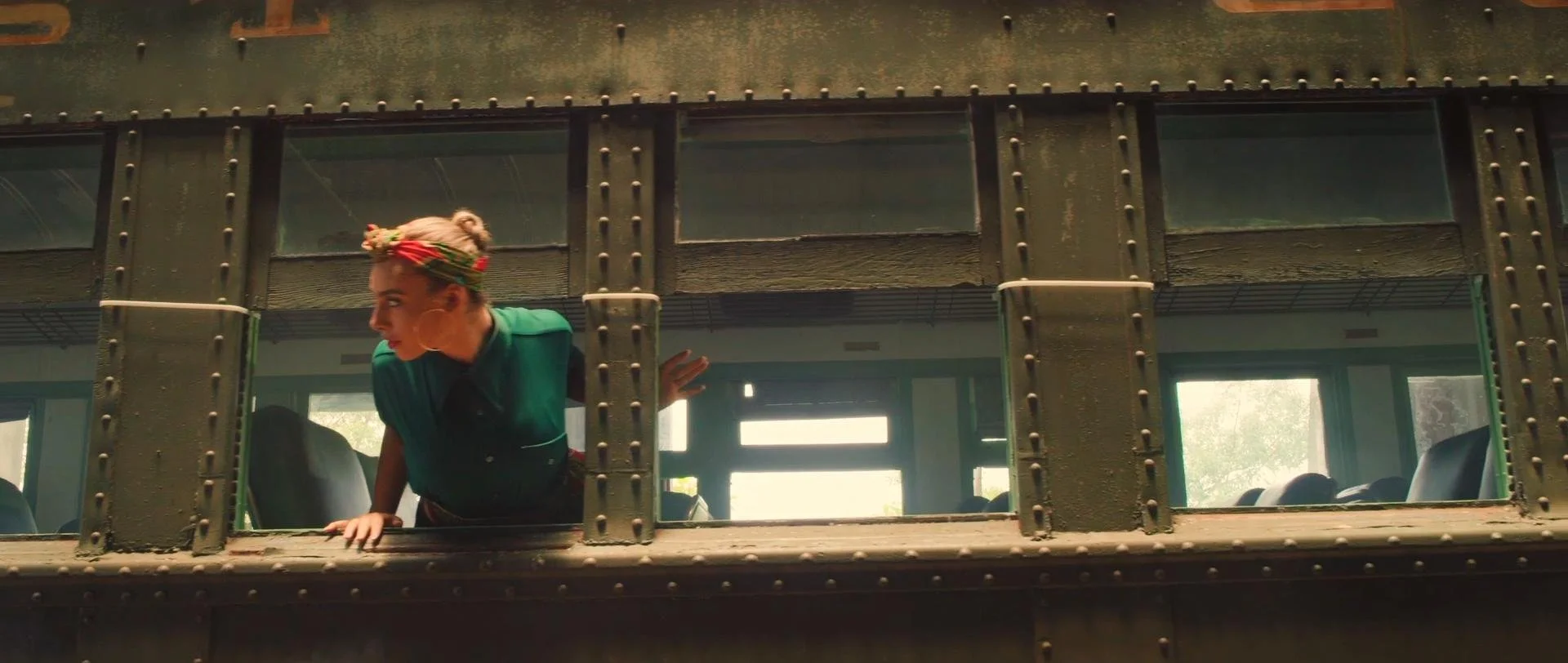 A woman with blonde hair and a headscarf peeking out of a window of an old train car.
