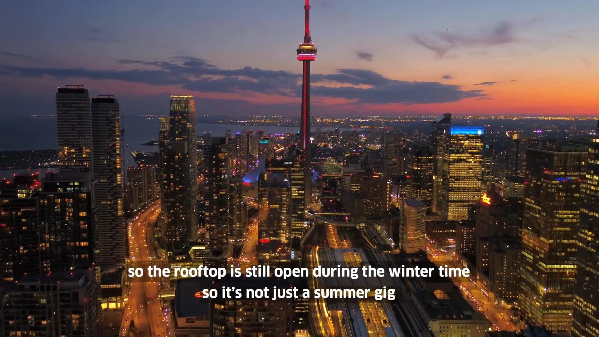Nighttime city skyline with illuminated buildings and the CN Tower in Toronto, Canada, under a sunset sky.