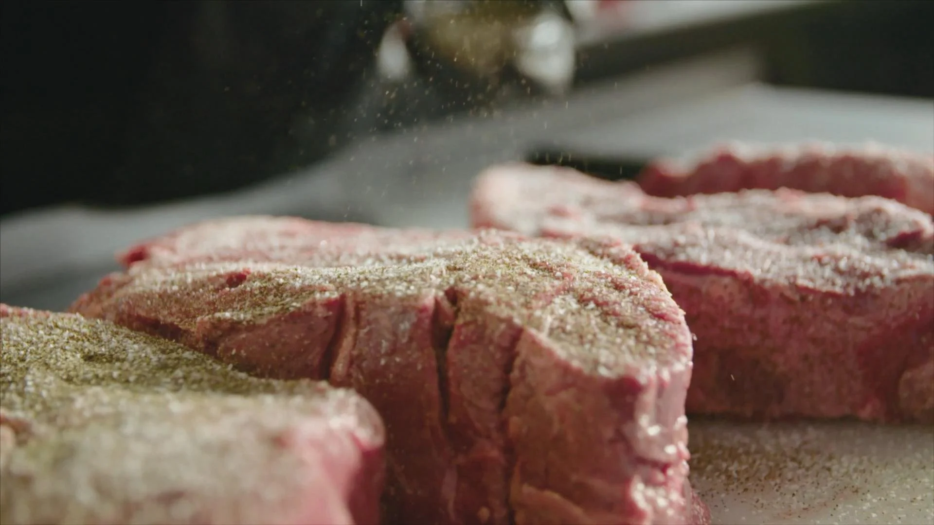 Cooking steaks seasoned with spices, being prepared on a grill.